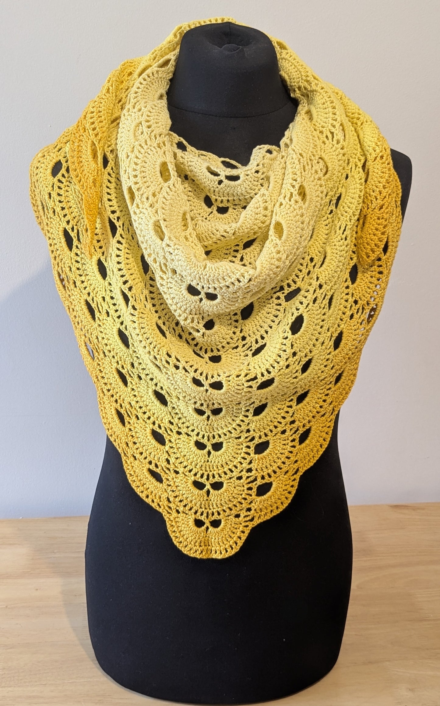 Yellow crocheted shawl on a black mannequin against a plain background