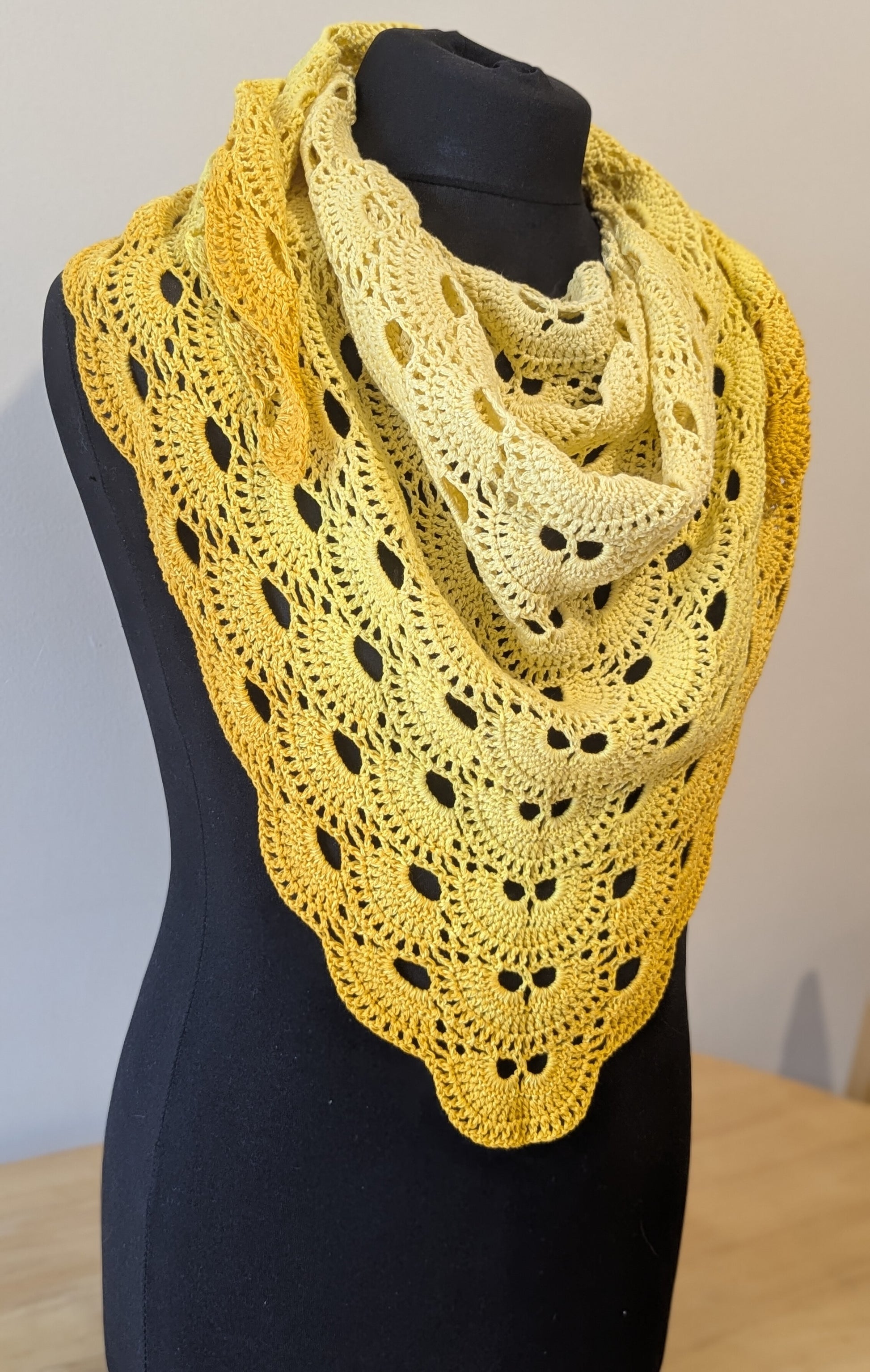 Yellow lace shawl on a mannequin against a plain background