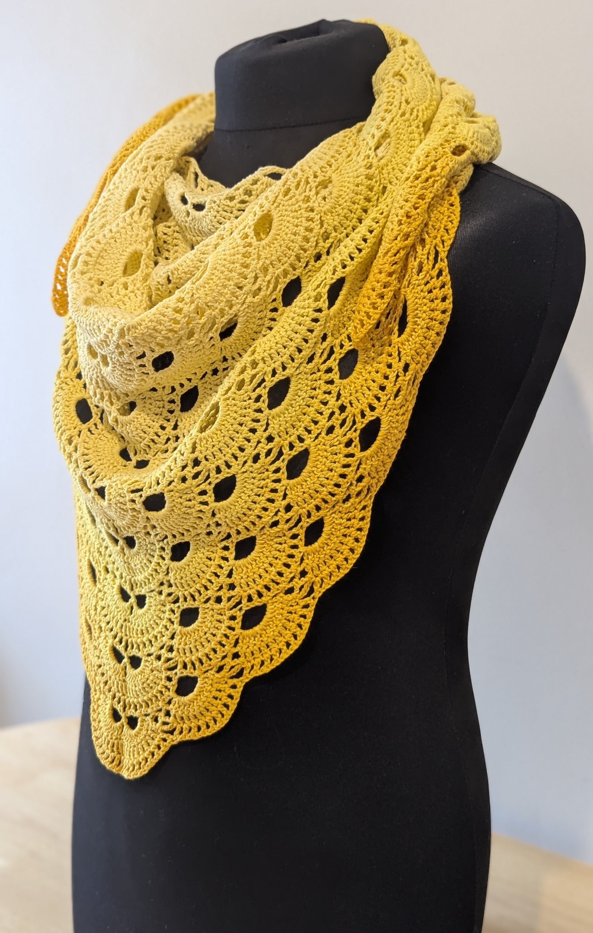 Yellow crocheted shawl on a mannequin against a white background