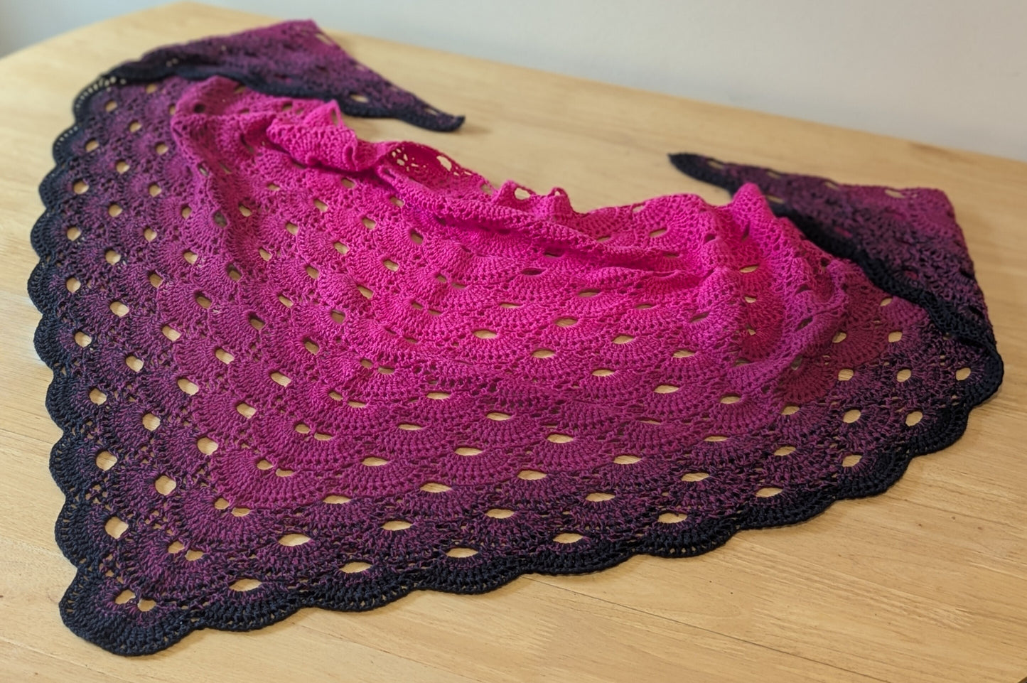 Crocheted shawl with a pink and black gradient on a wooden surface