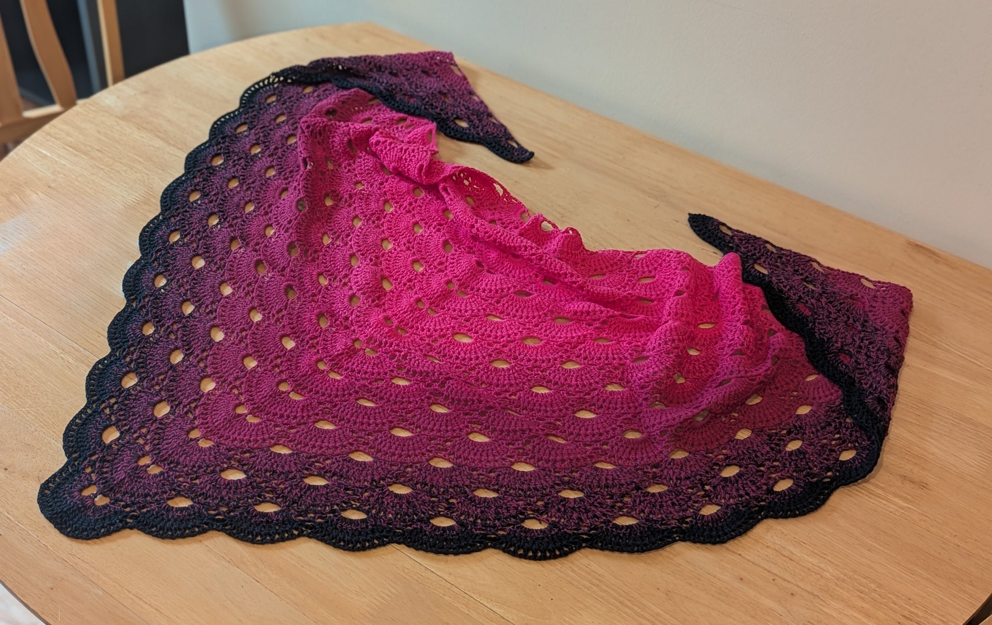 Crochet shawl with pink and black gradient on a wooden surface