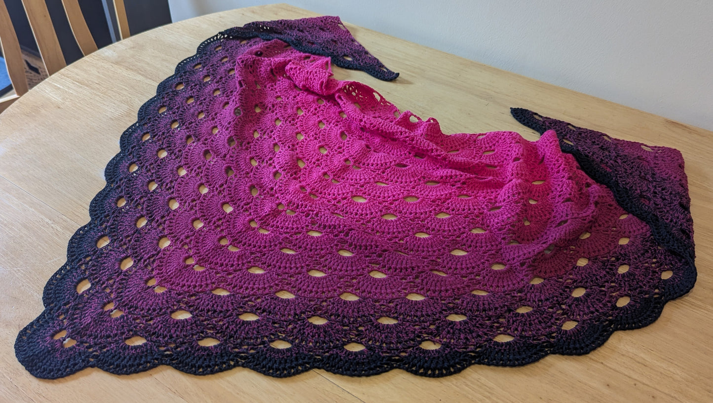 Crocheted shawl with a pink and black gradient on a wooden surface