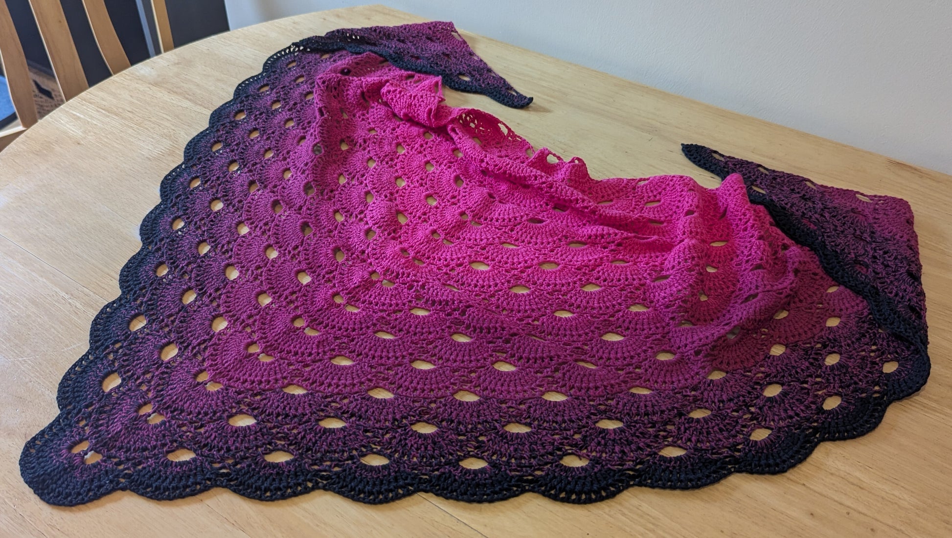 Crocheted shawl with a pink and black gradient on a wooden surface