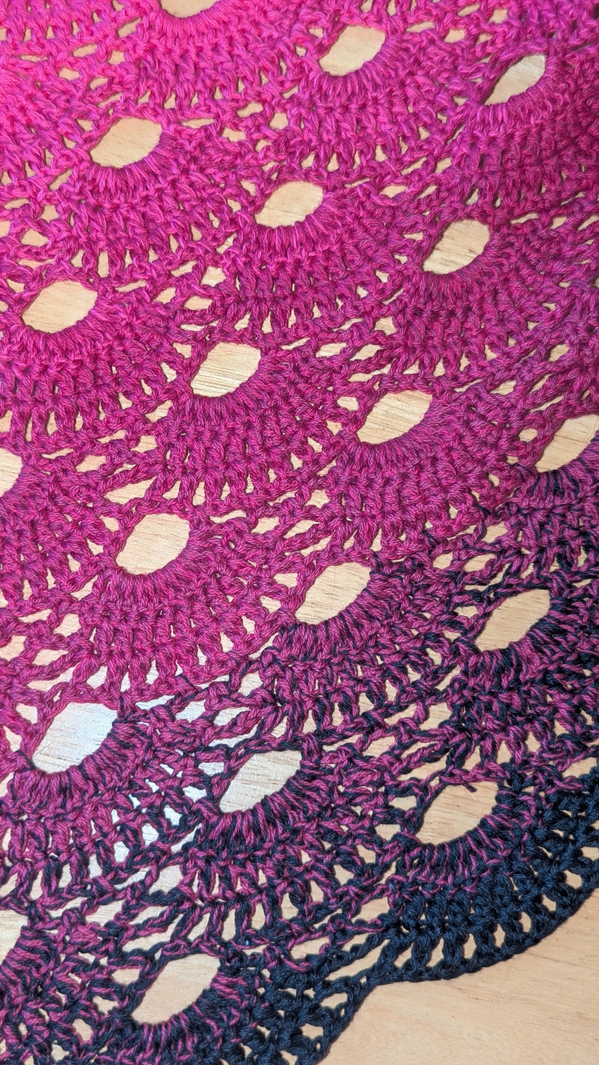 Close-up of a pink and black crocheted shawl with a gradient  pattern