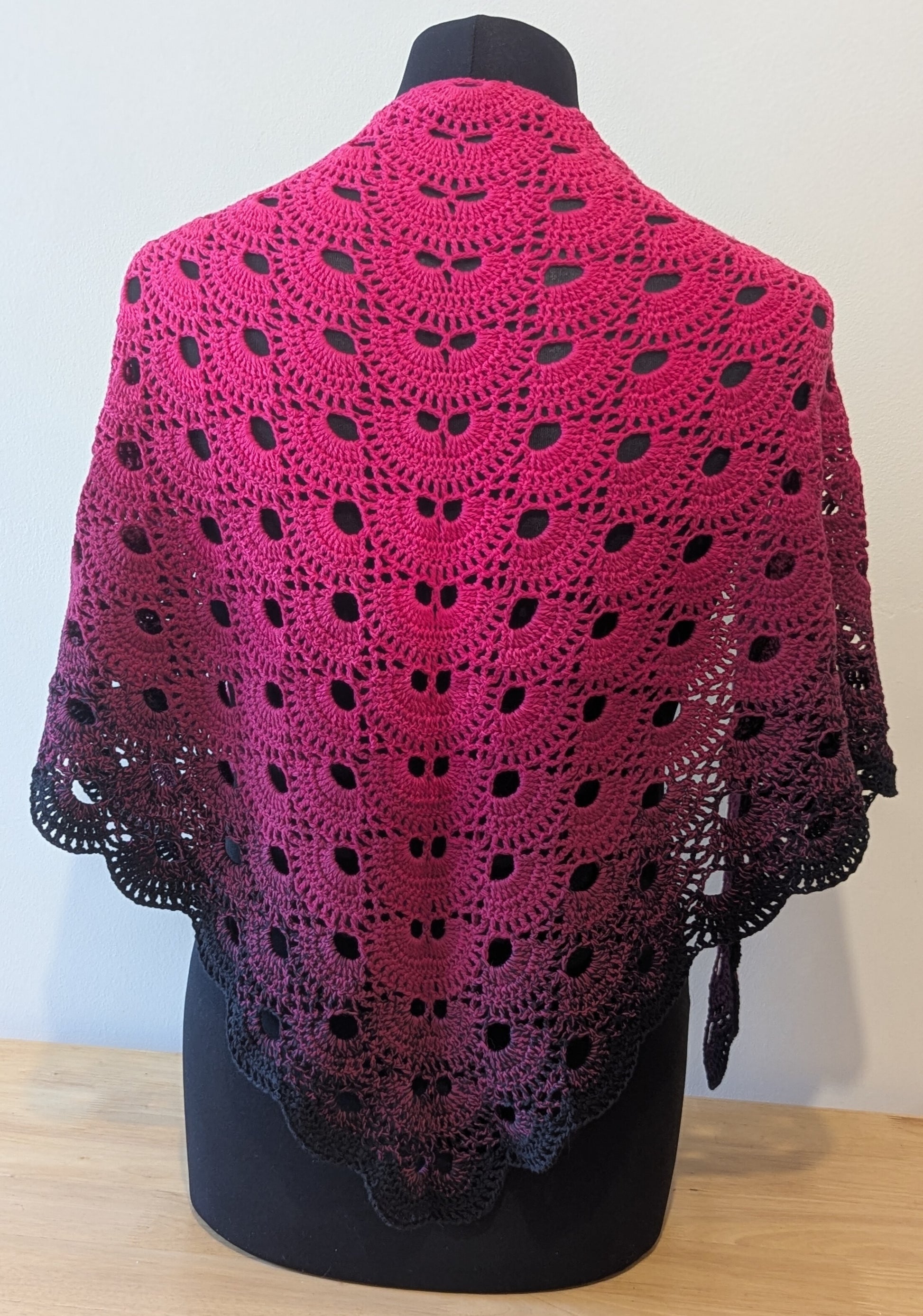 Pink and black crocheted shawl on a mannequin against a white background