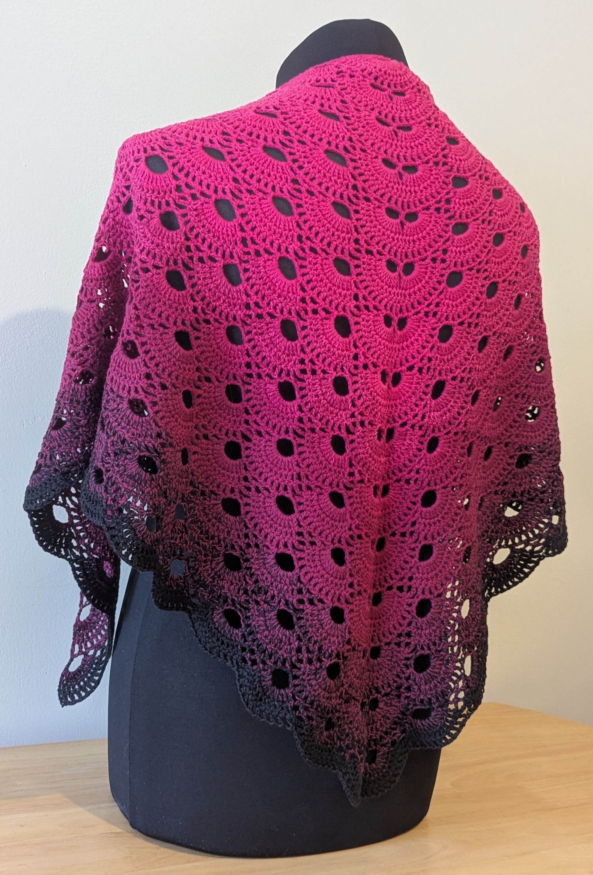 Pink and black crocheted shawl on a mannequin against a plain background