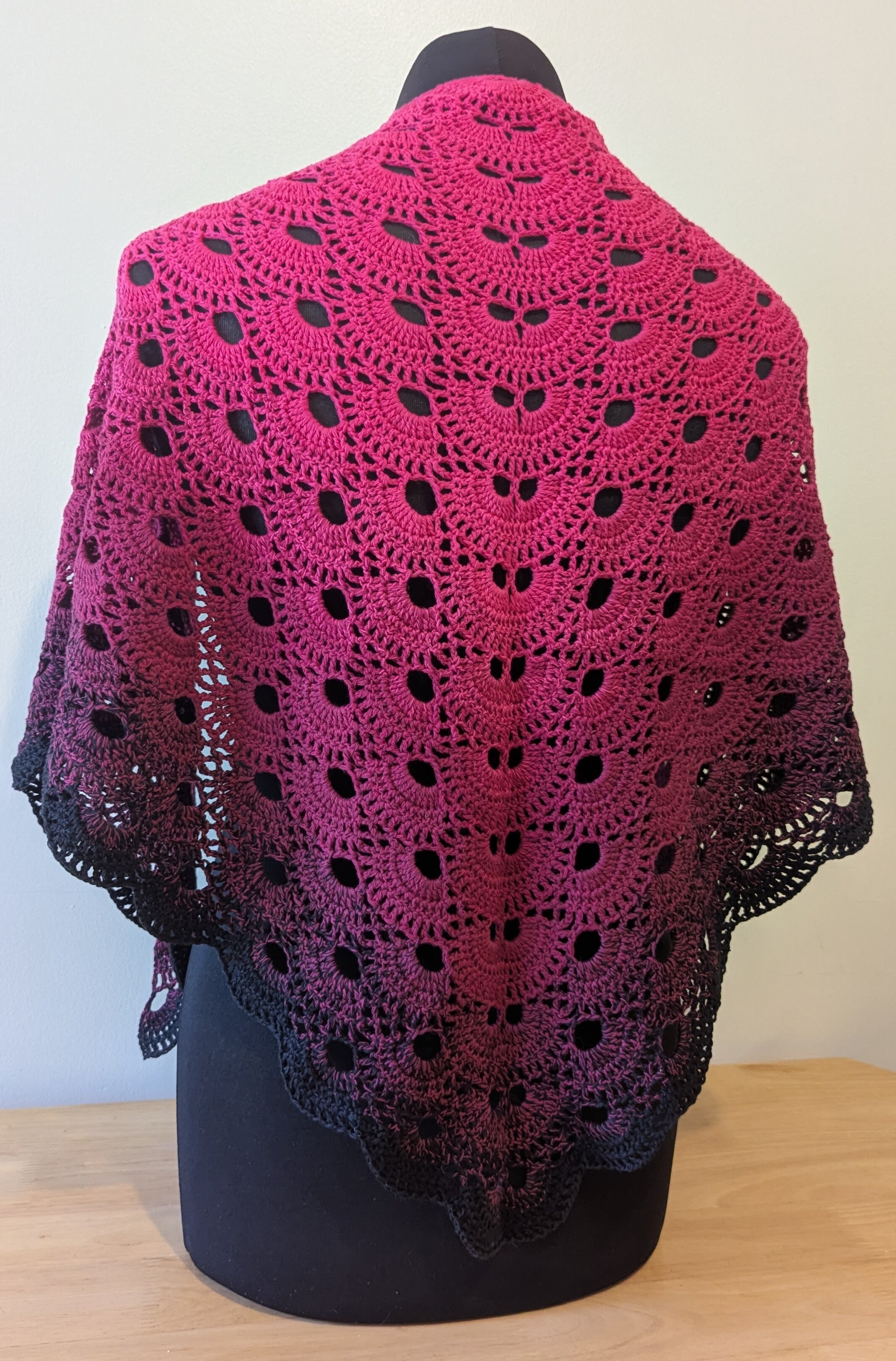 Crocheted shawl with a gradient of pink and black on a mannequin against a plain background