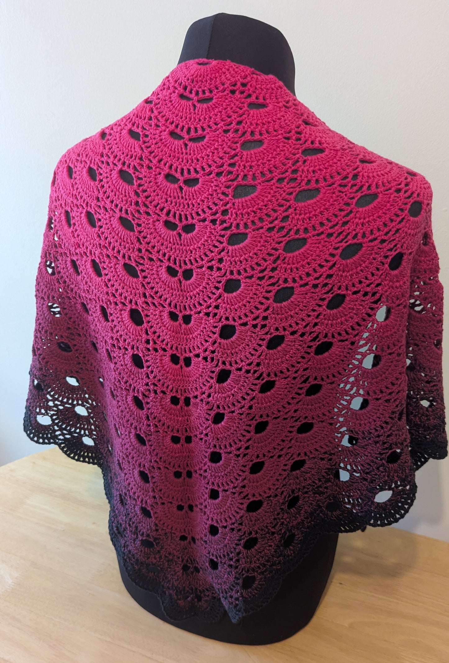 Pink crochet shawl on a mannequin against a white background