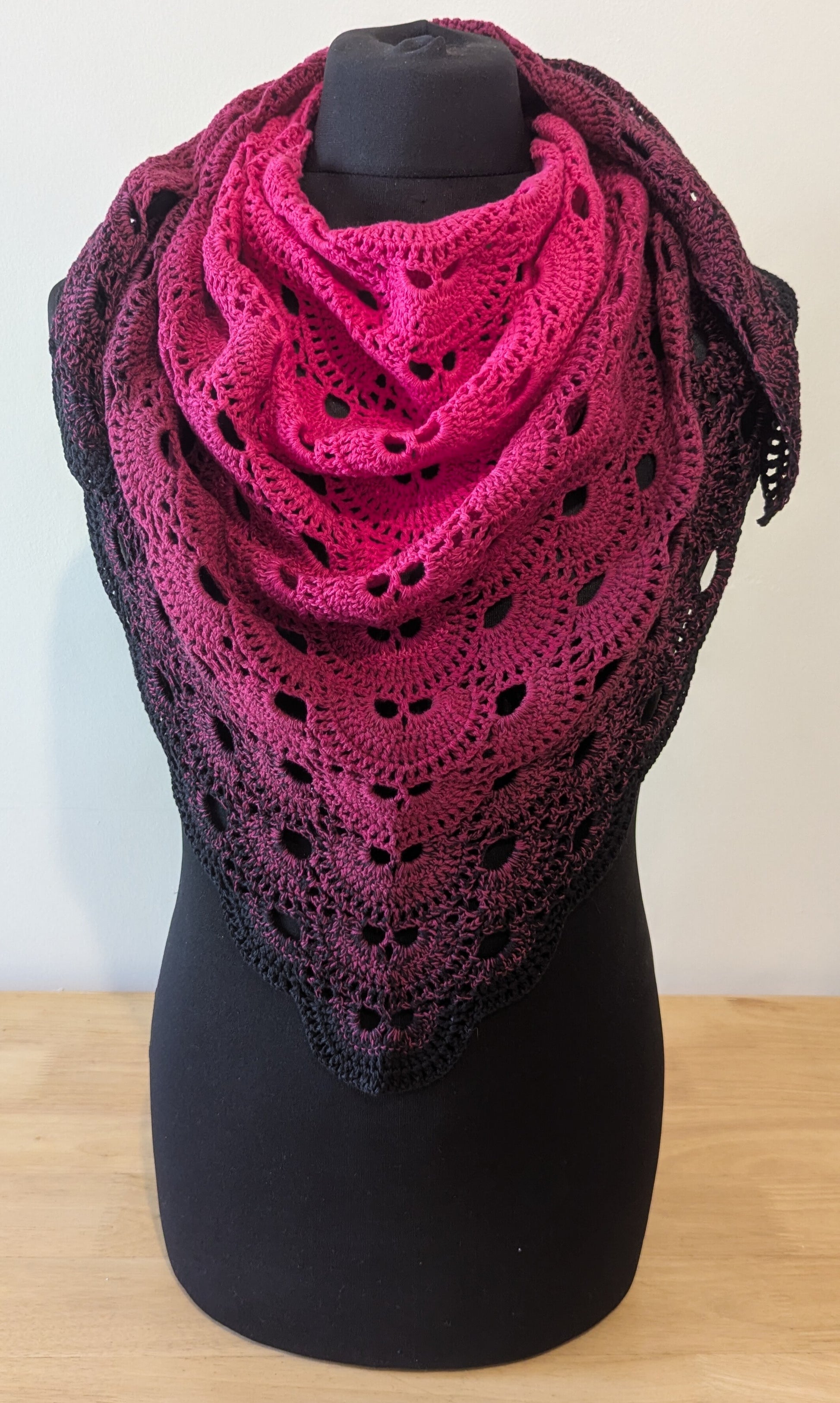 Pink and black lace shawl on a black mannequin against a white background