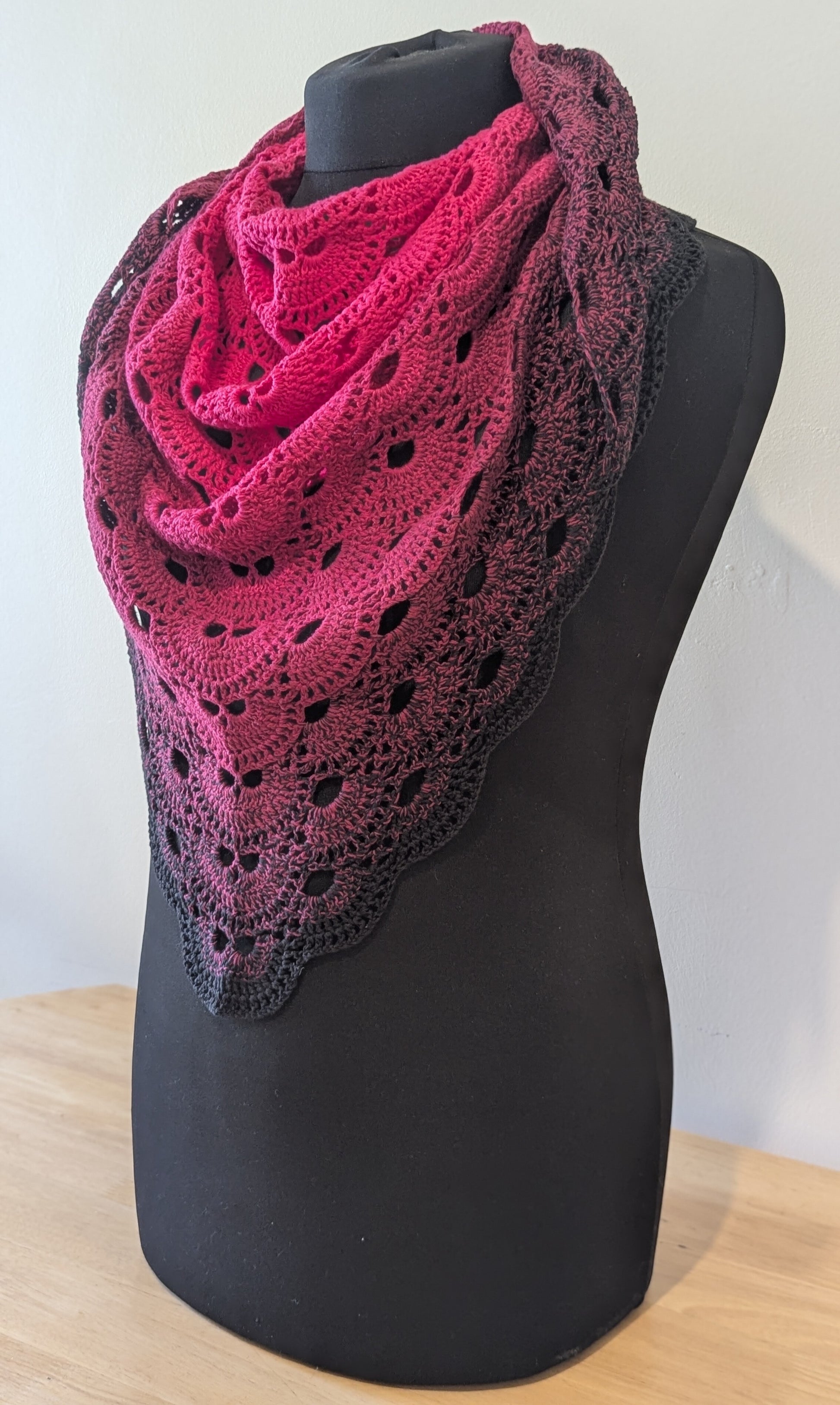 Pink and black crocheted shawl on a black mannequin against a white background