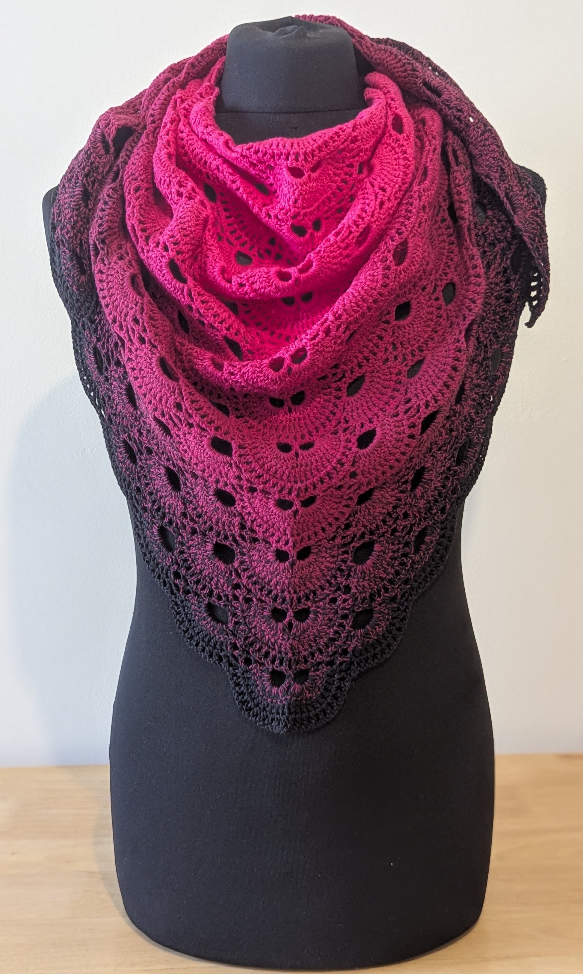 Pink crochet shawl on a black mannequin against a white background
