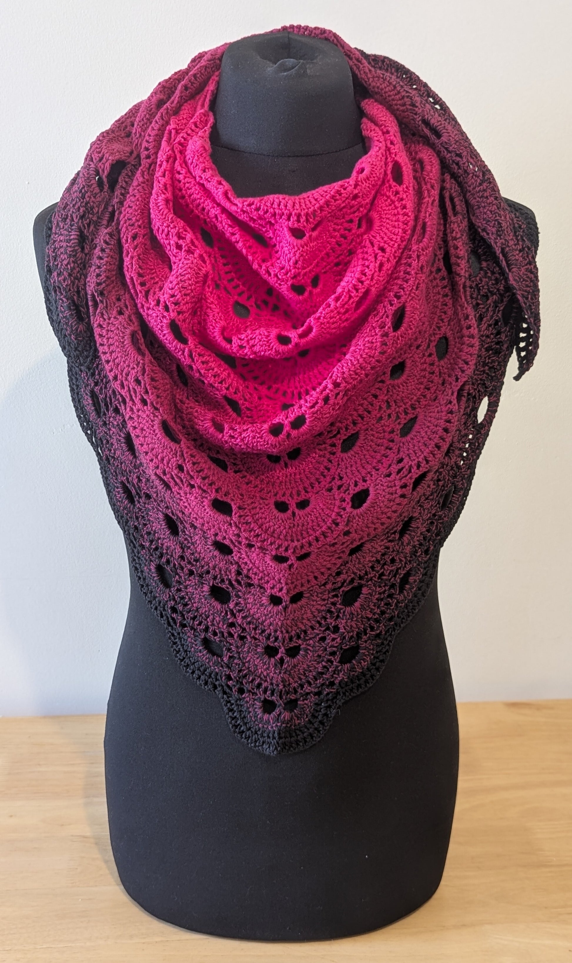 Pink and black crocheted shawl on a black mannequin against a white background