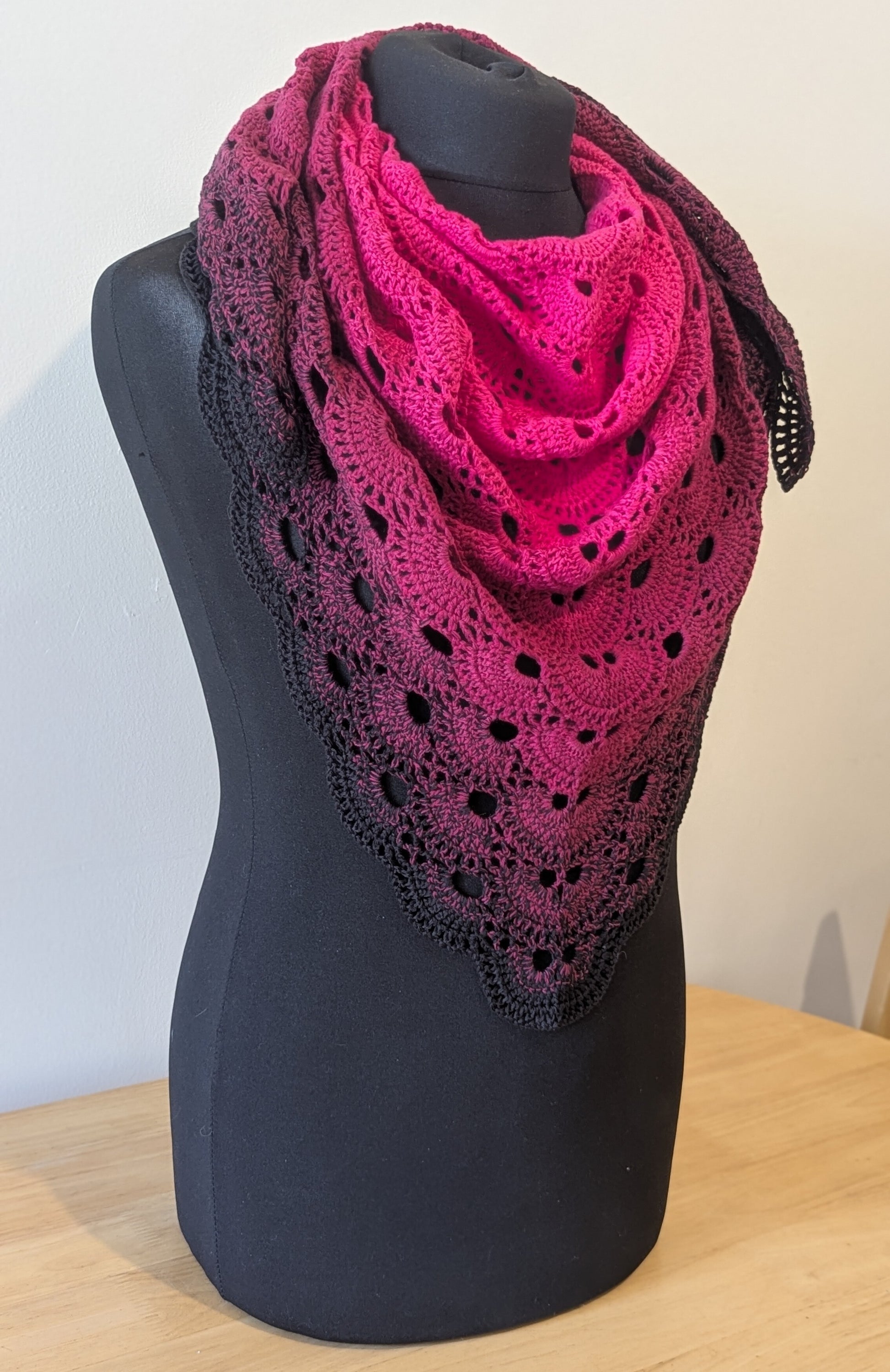 Pink and black crocheted shawl on a black mannequin against a white background