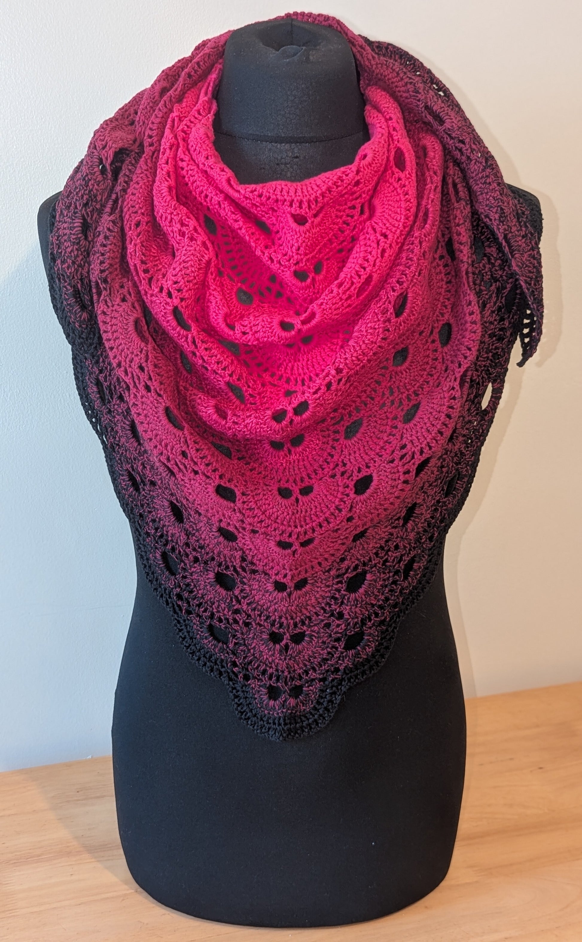 Pink and black crocheted shawl on a mannequin against a plain background