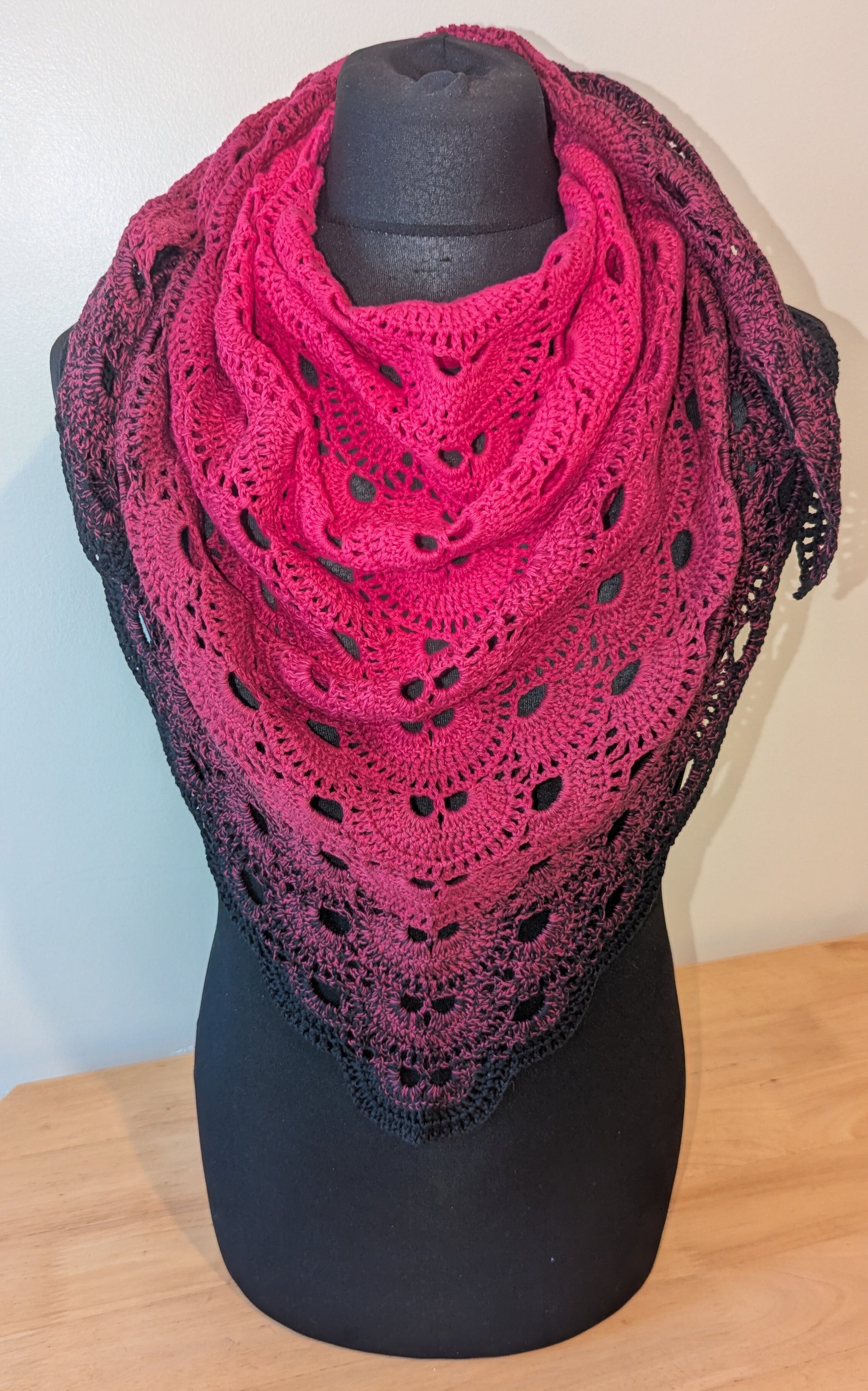 Pink crochet shawl on a black mannequin against a white wall.