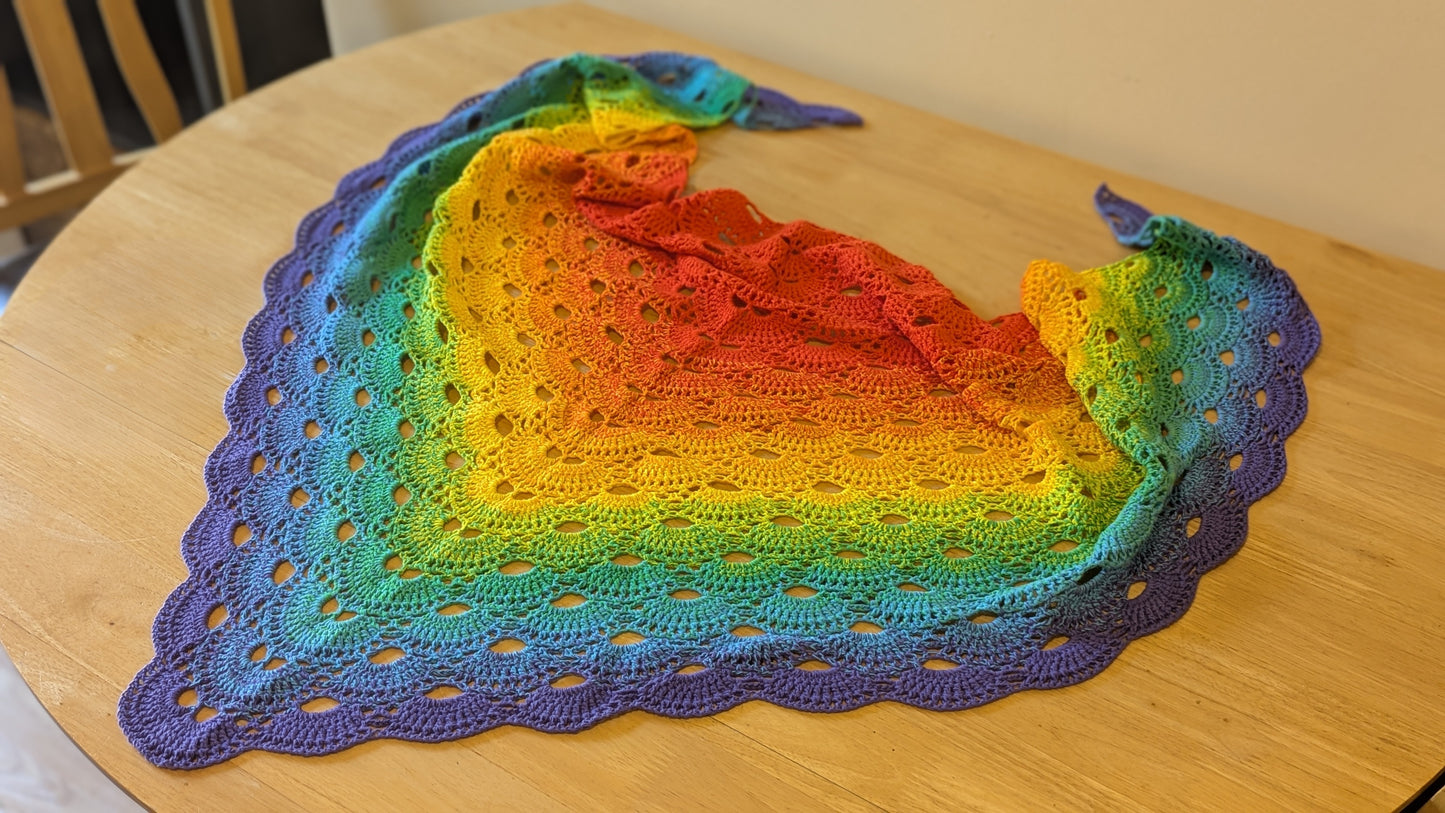 Colorful crocheted shawl with a gradient pattern on a wooden surface