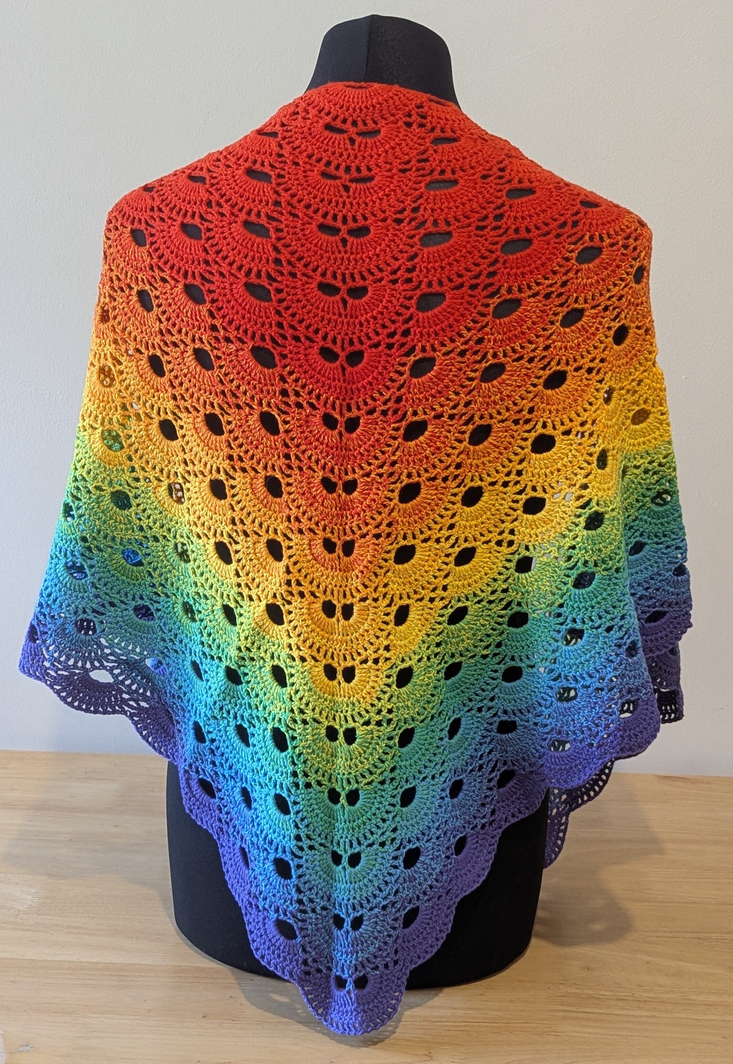 Rainbow-colored crocheted shawl on a mannequin against a white background