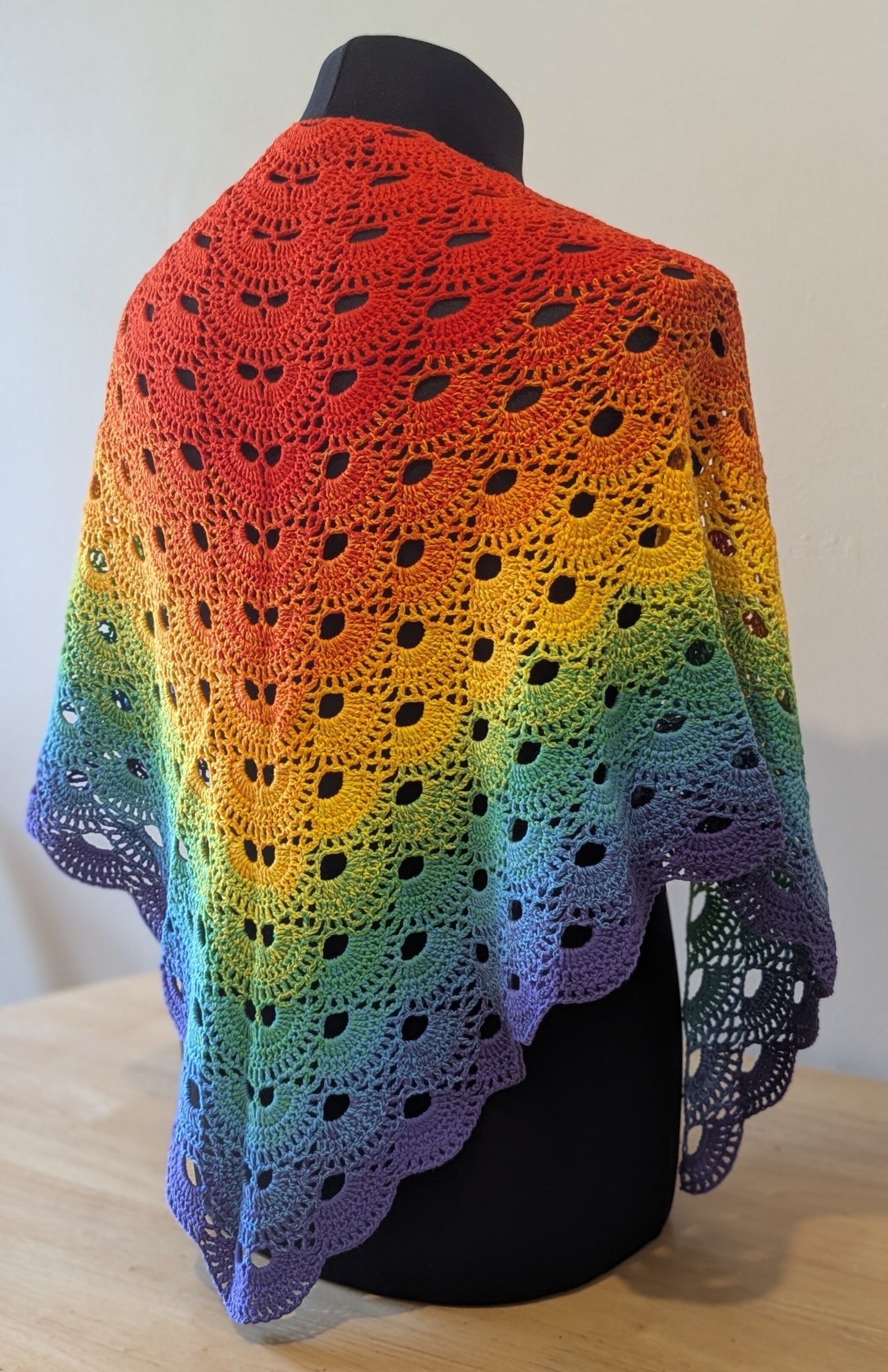 Rainbow-colored crocheted shawl on a mannequin against a white background