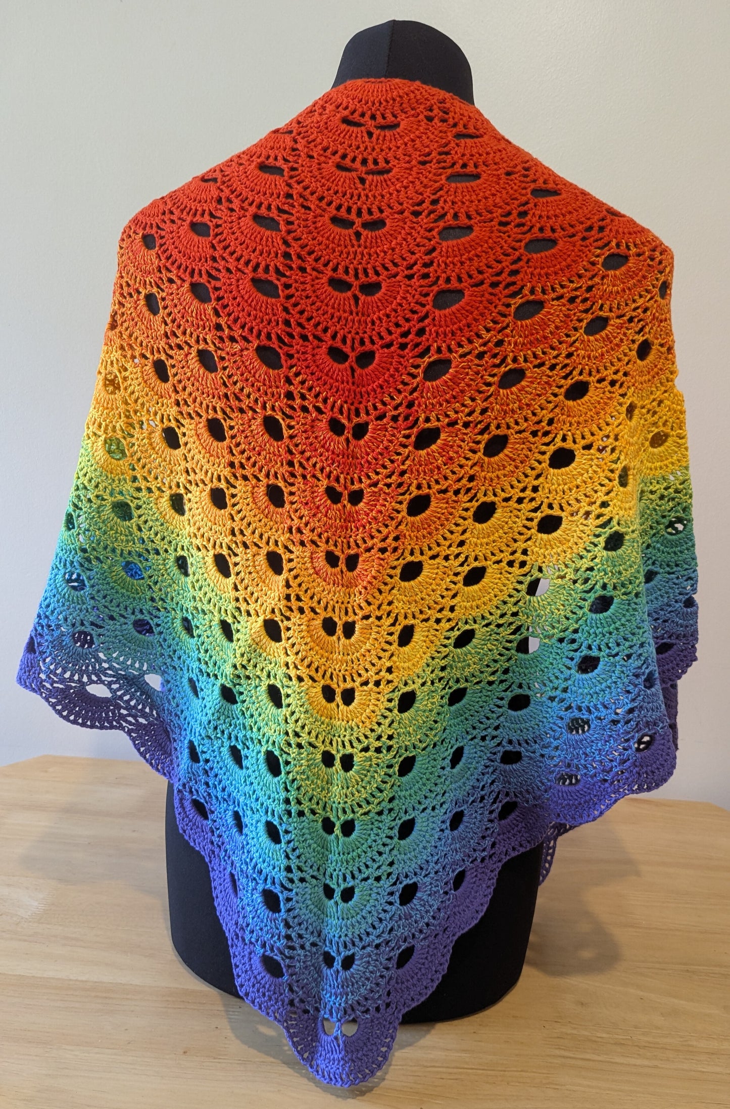 Colorful crocheted shawl with a gradient pattern on a mannequin against a plain background.