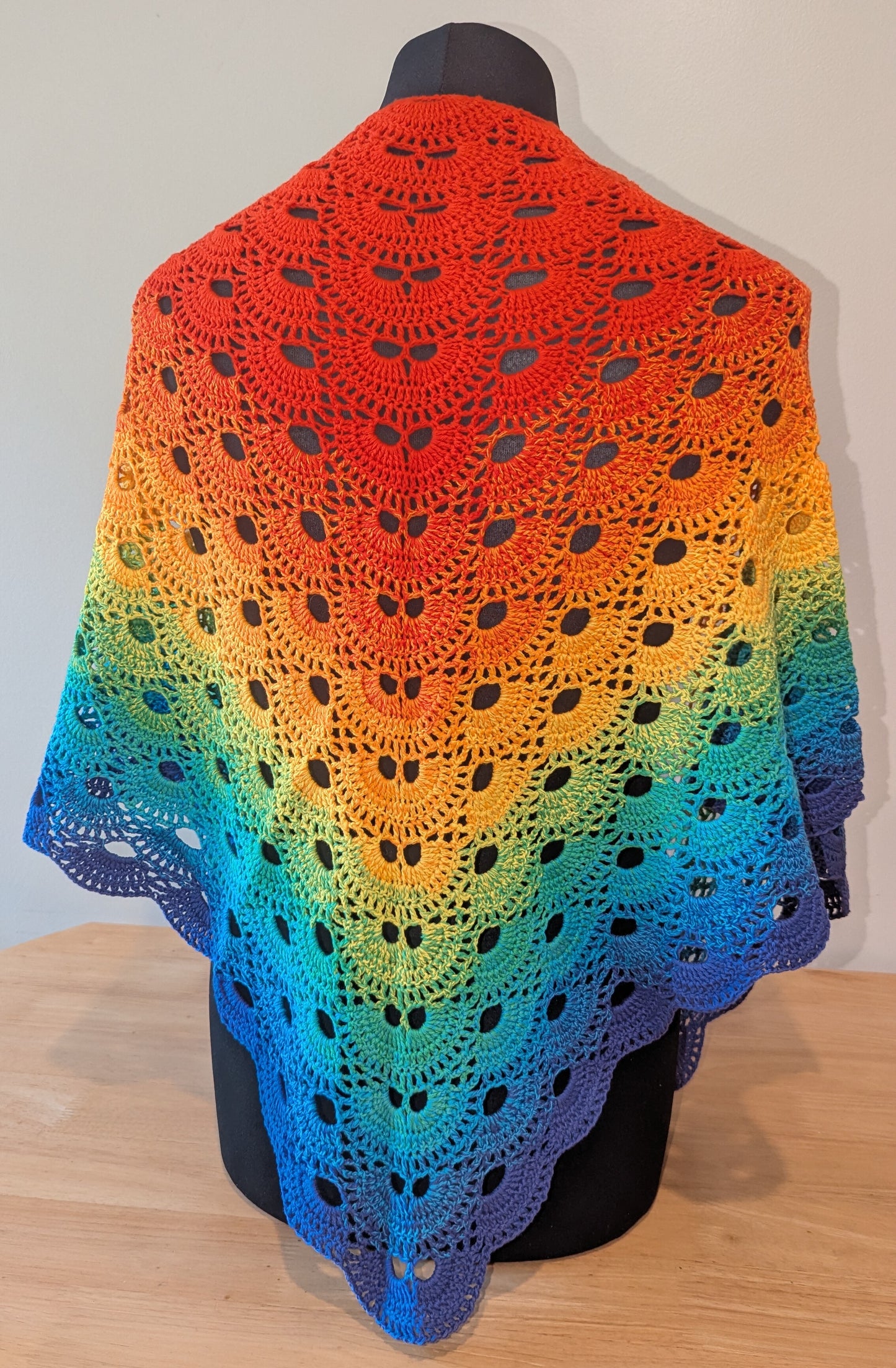 Colorful crocheted shawl with a gradient pattern on a mannequin against a neutral background.