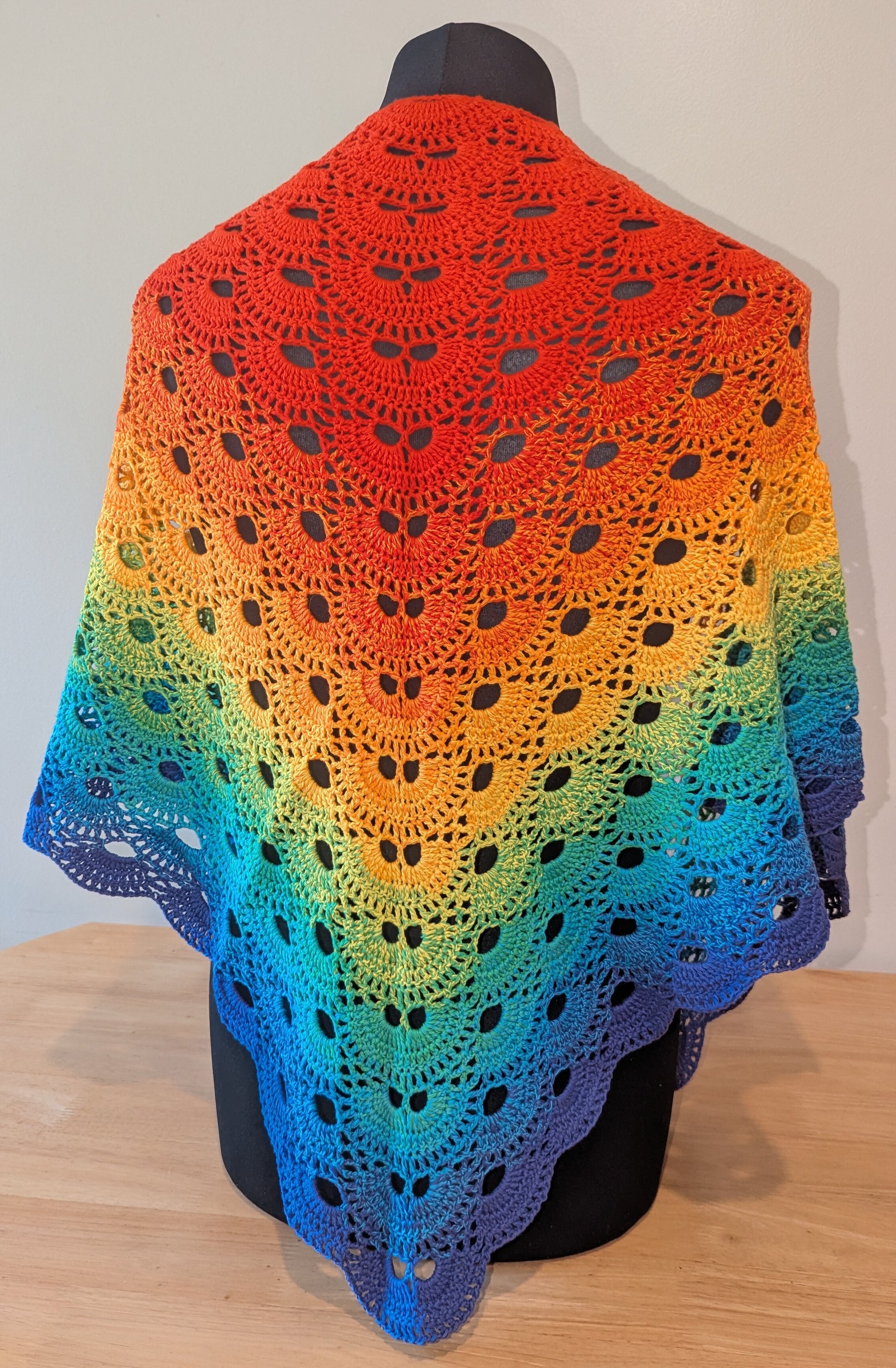Colorful crocheted shawl with a gradient pattern on a mannequin against a neutral background.
