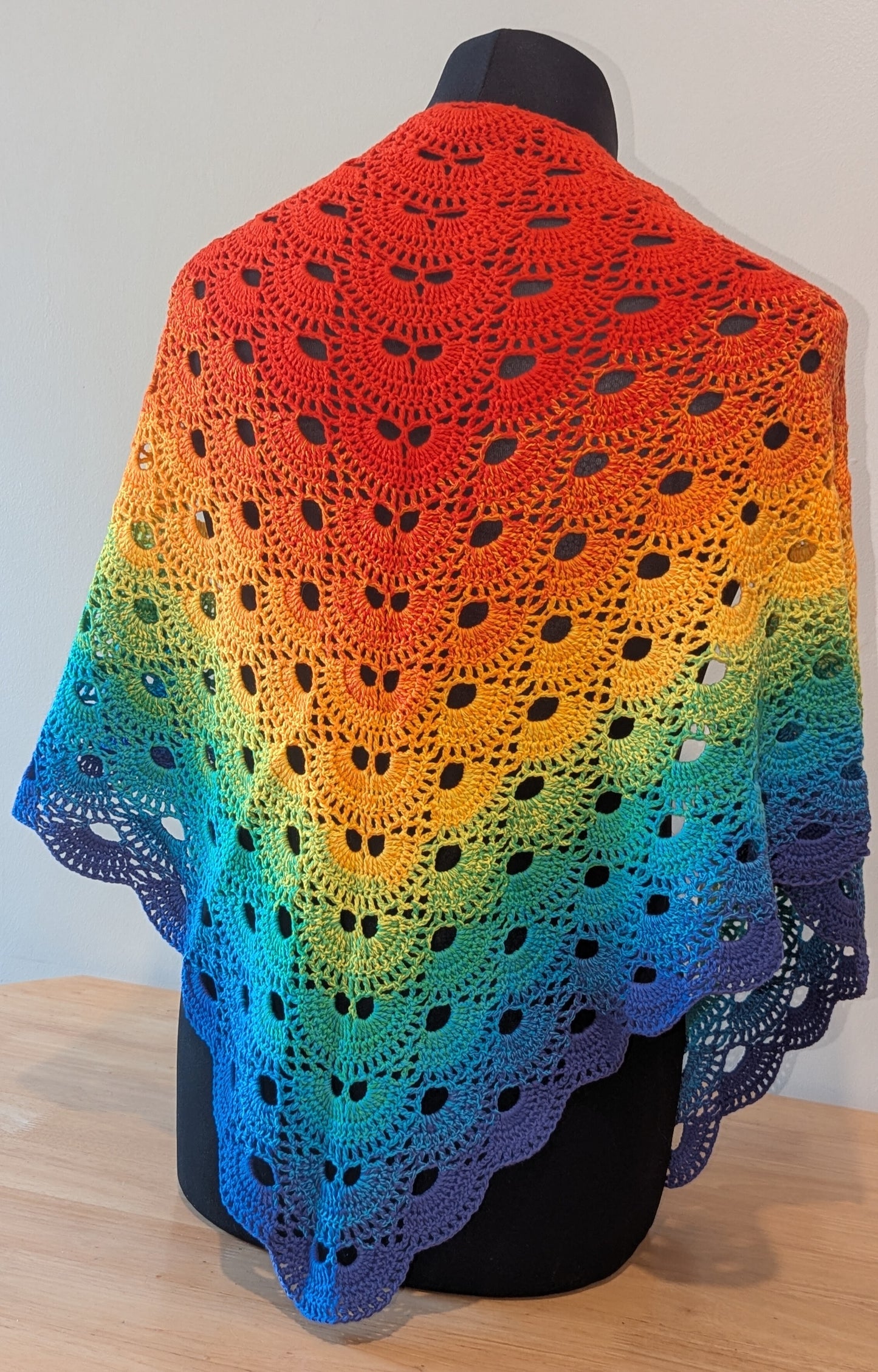 Colorful crocheted shawl with a gradient pattern on a mannequin against a white background.