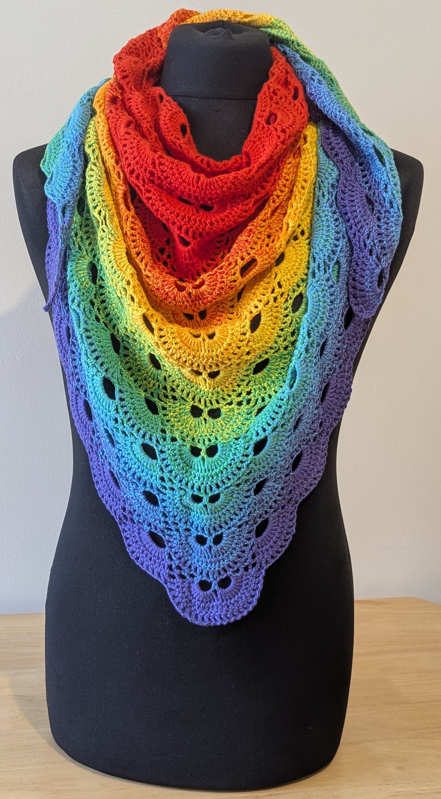 Rainbow-colored crocheted shawl on a mannequin against a white background