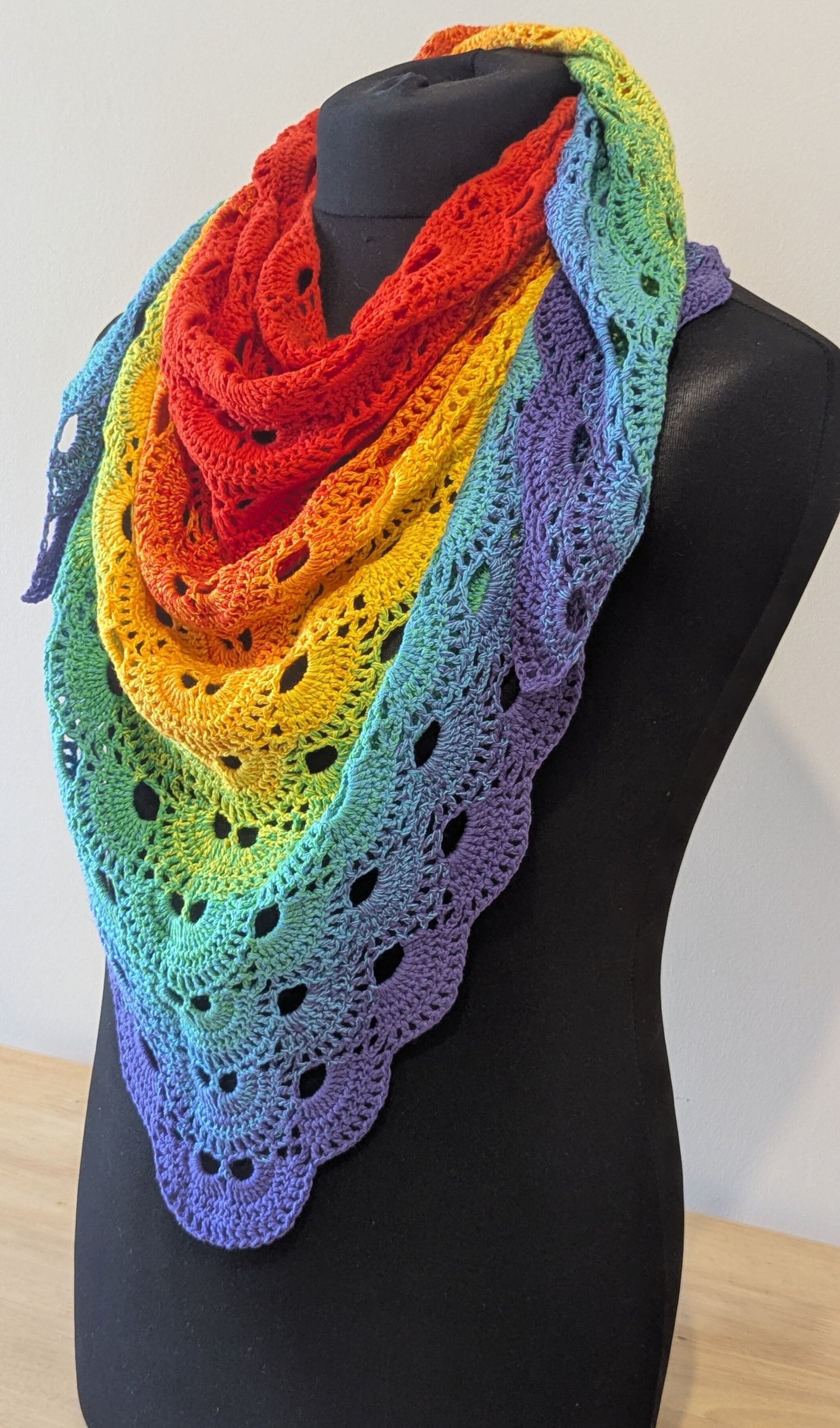 Rainbow-colored crocheted shawl on a mannequin against a white background