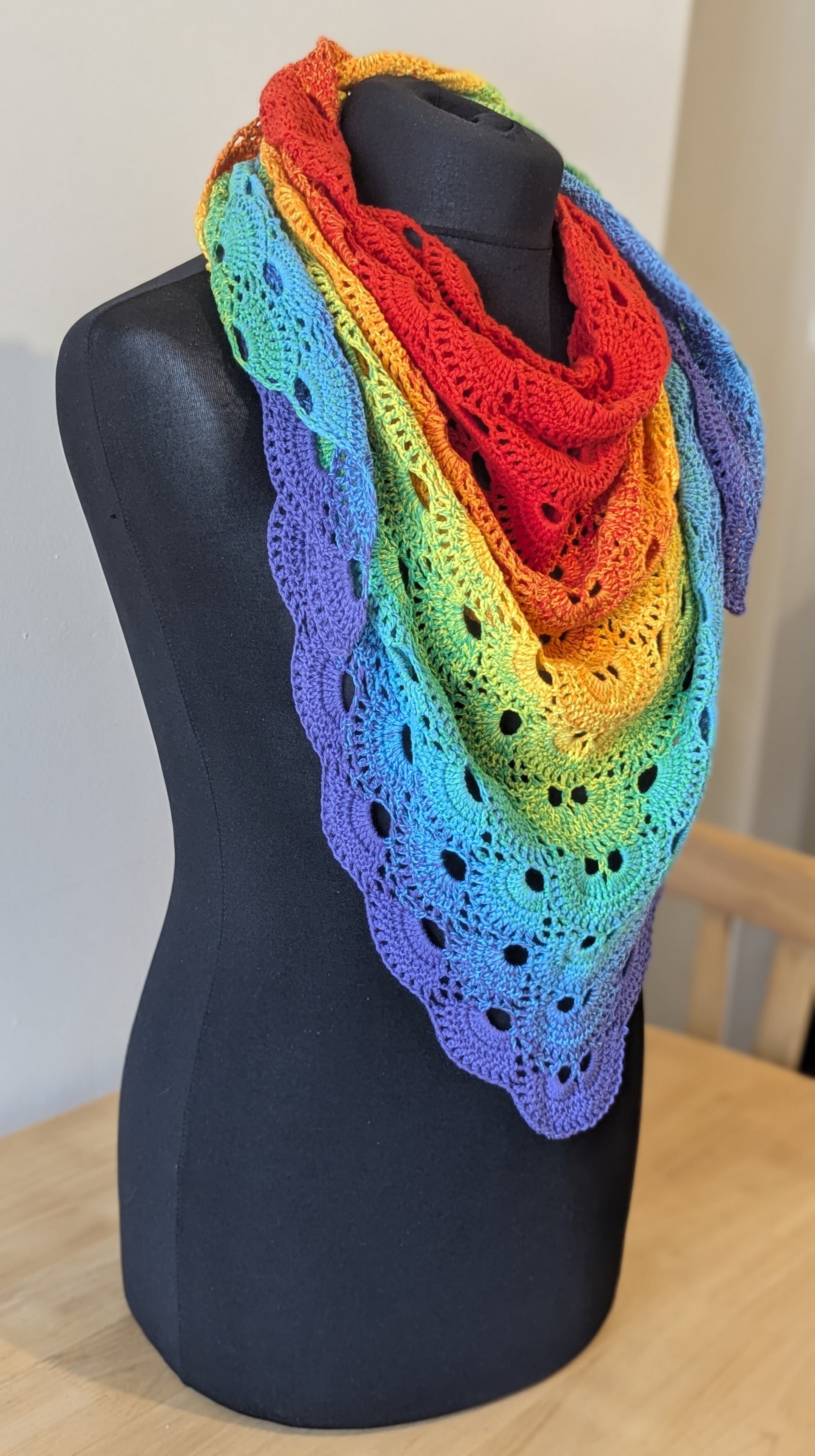 Rainbow-colored shawl on a black mannequin against a neutral background