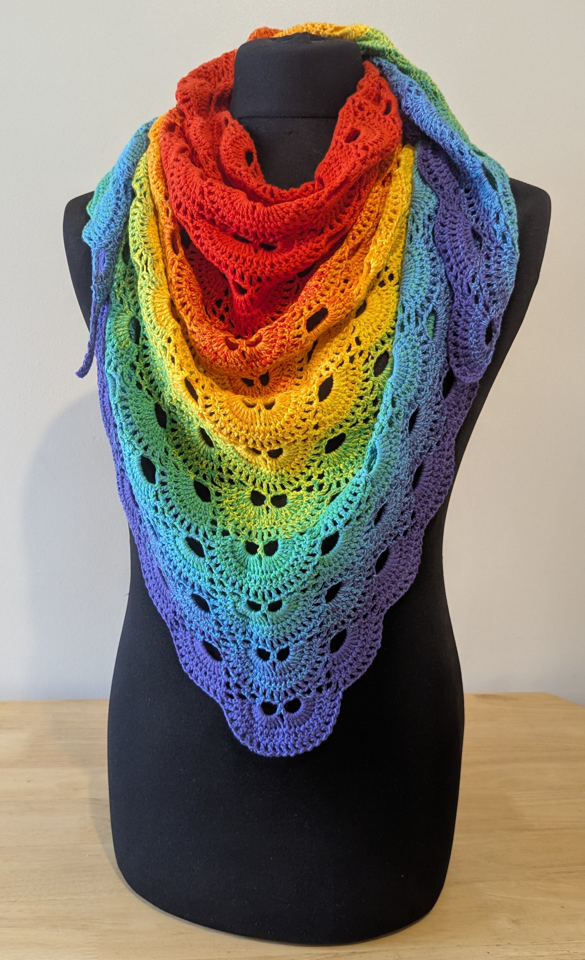 Rainbow-colored shawl on a mannequin against a plain background