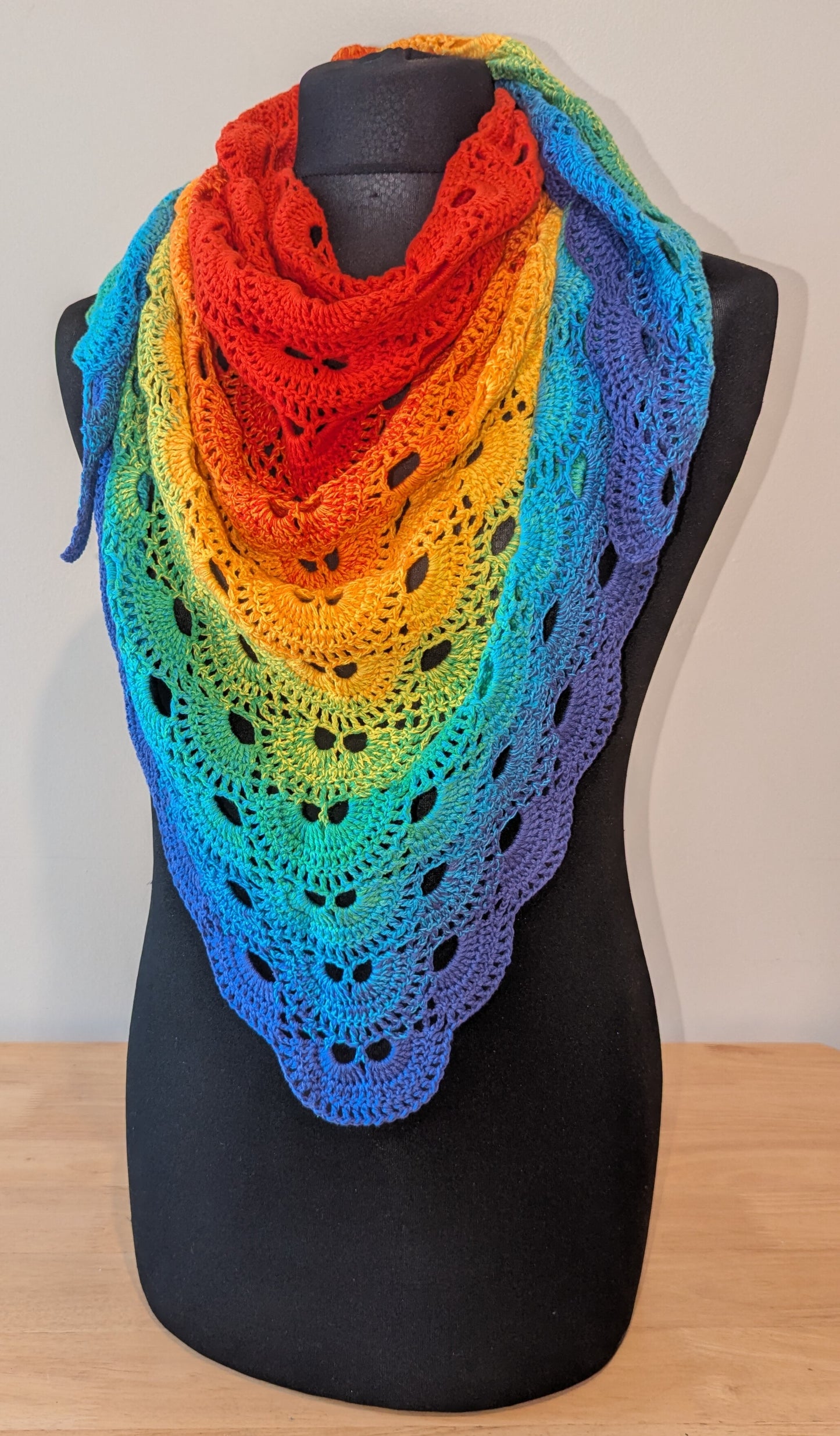 Rainbow-colored shawl on a mannequin against a plain background