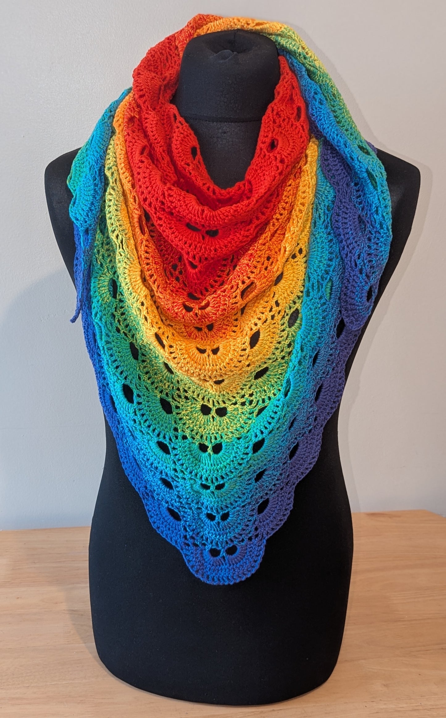 Rainbow-colored crochet shawl on a black mannequin against a white background