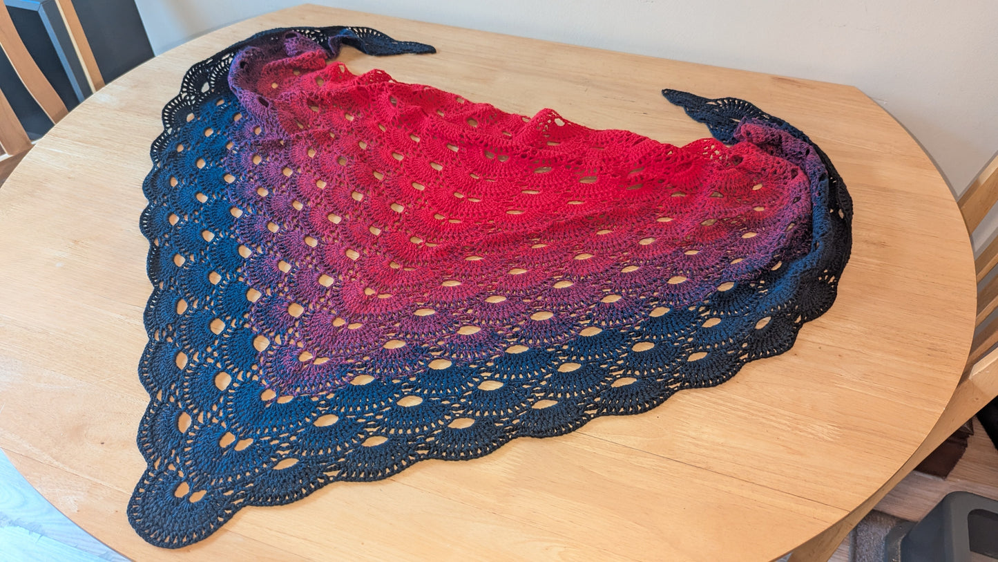 Red and black gradient crocheted shawl  on a wooden table.