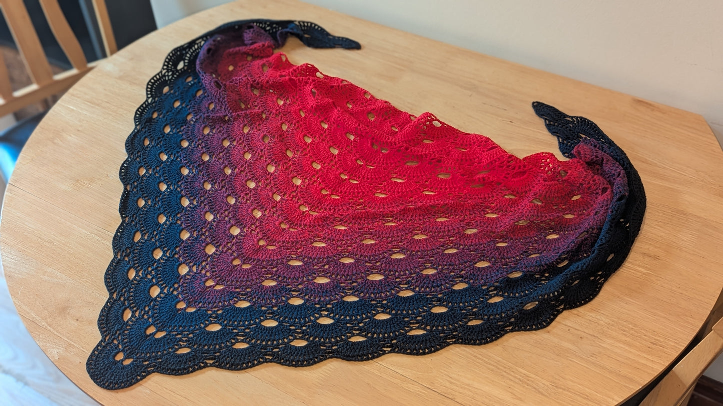 Crochet shawl with a gradient of red to black on a wooden surface