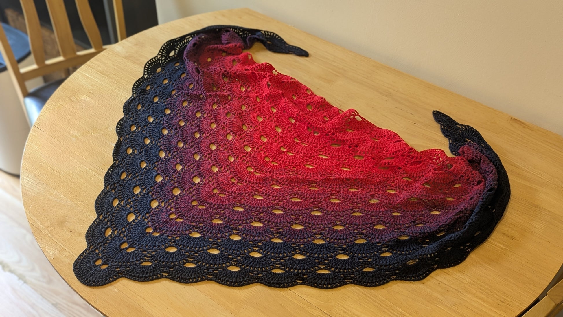Crochet shawl with gradient color pattern on a wooden surface