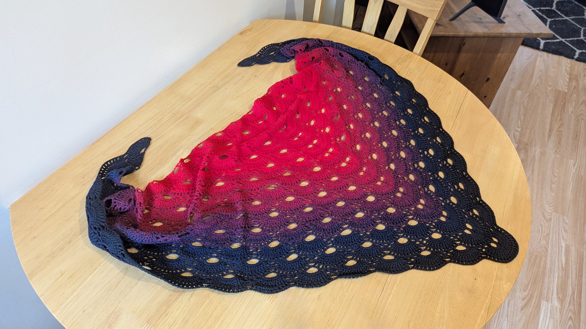 Crochet shawl with red and black pattern on a wooden table