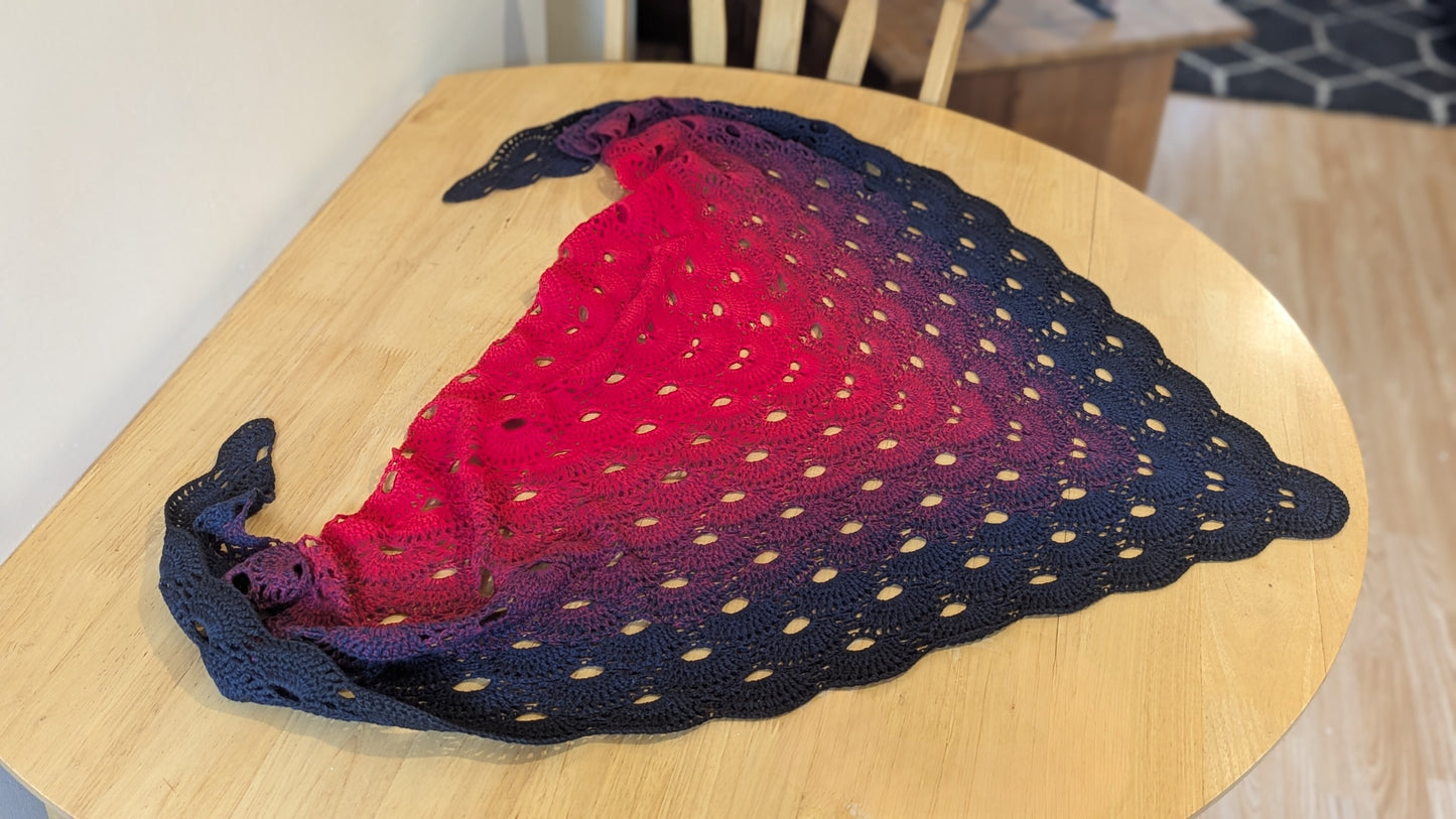 Crochet shawl with red and black gradient on a wooden table