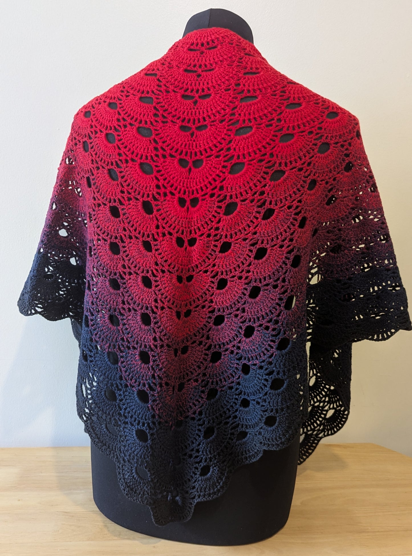 Red and black crocheted shawl on a mannequin against a white background