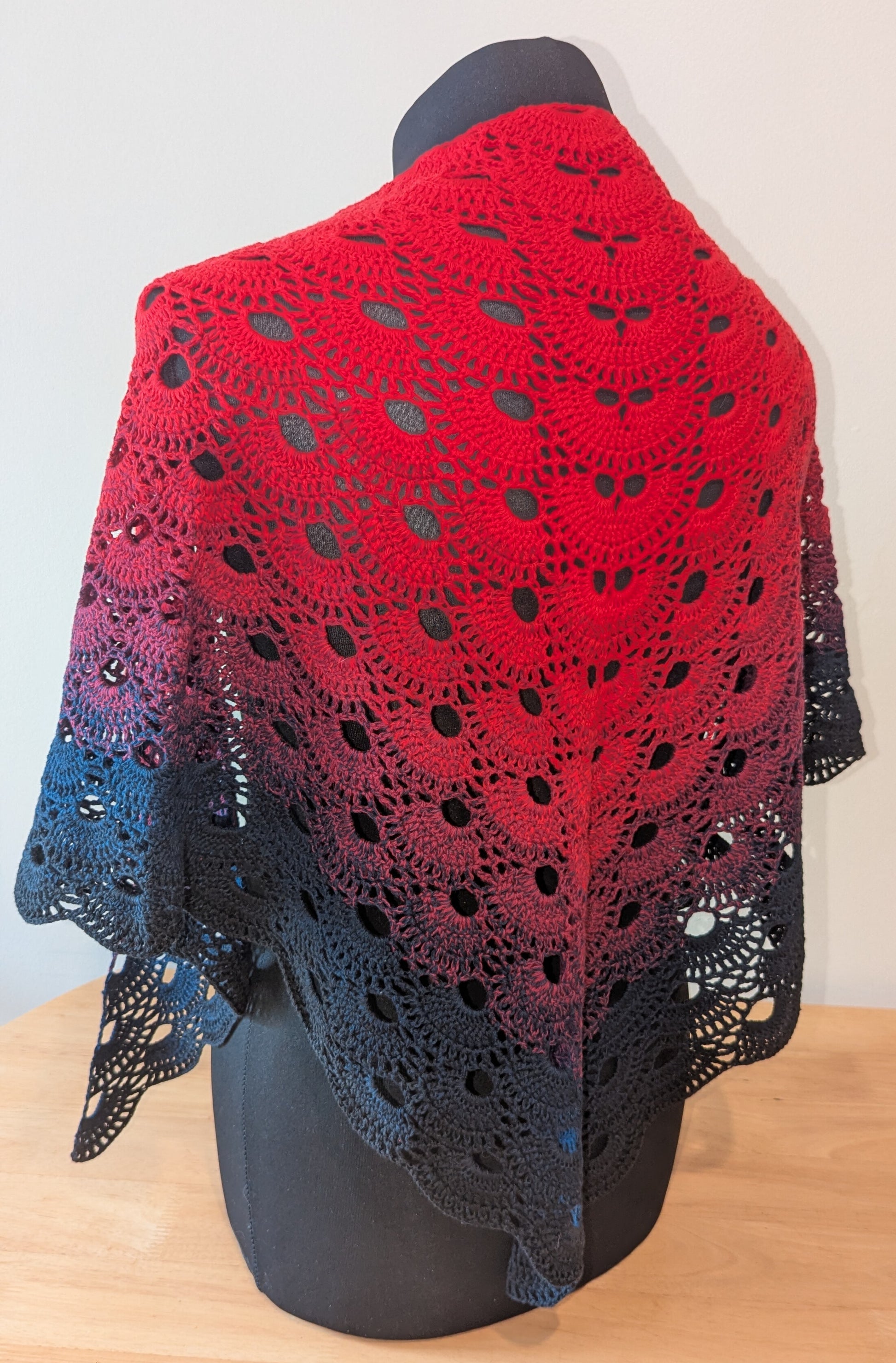 Red and black crocheted shawl on a mannequin against a white background
