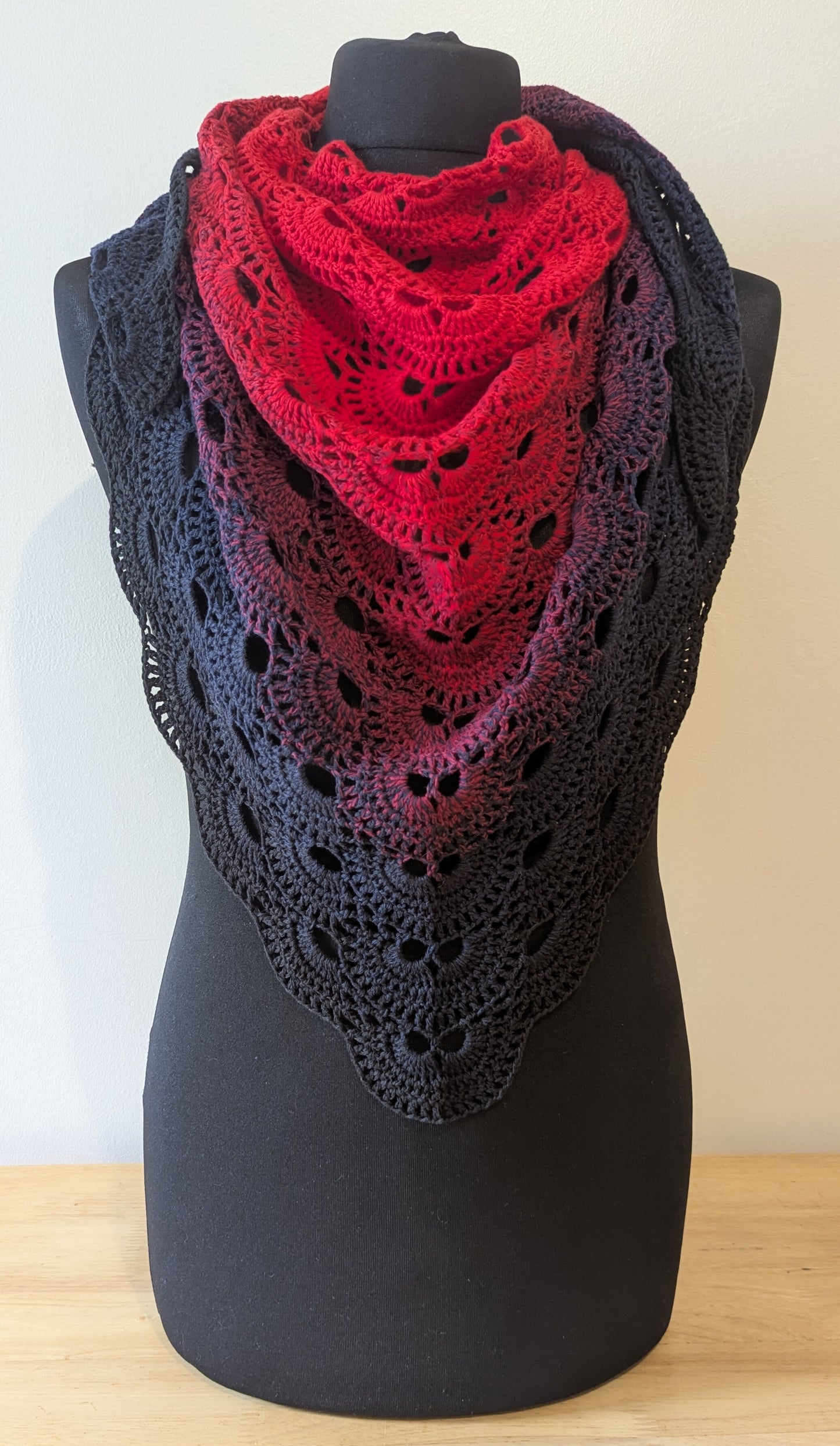 Red and black crocheted shawl on a mannequin against a beige background