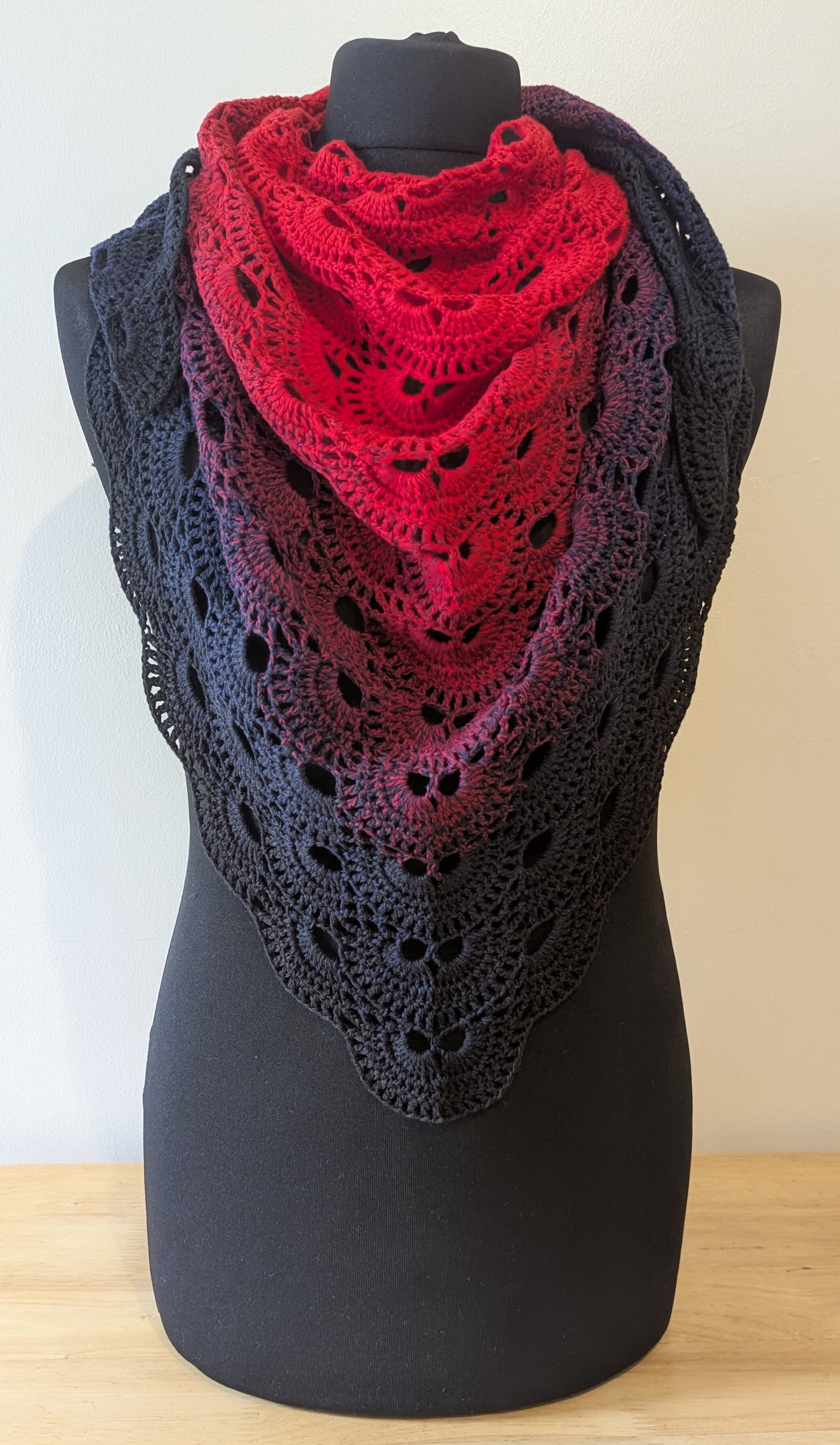 Red and black crocheted shawl on a mannequin against a beige background