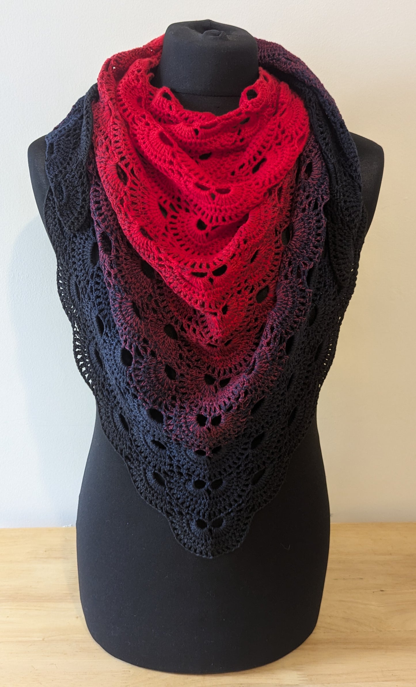 Red and black crocheted shawl on a mannequin against a white background