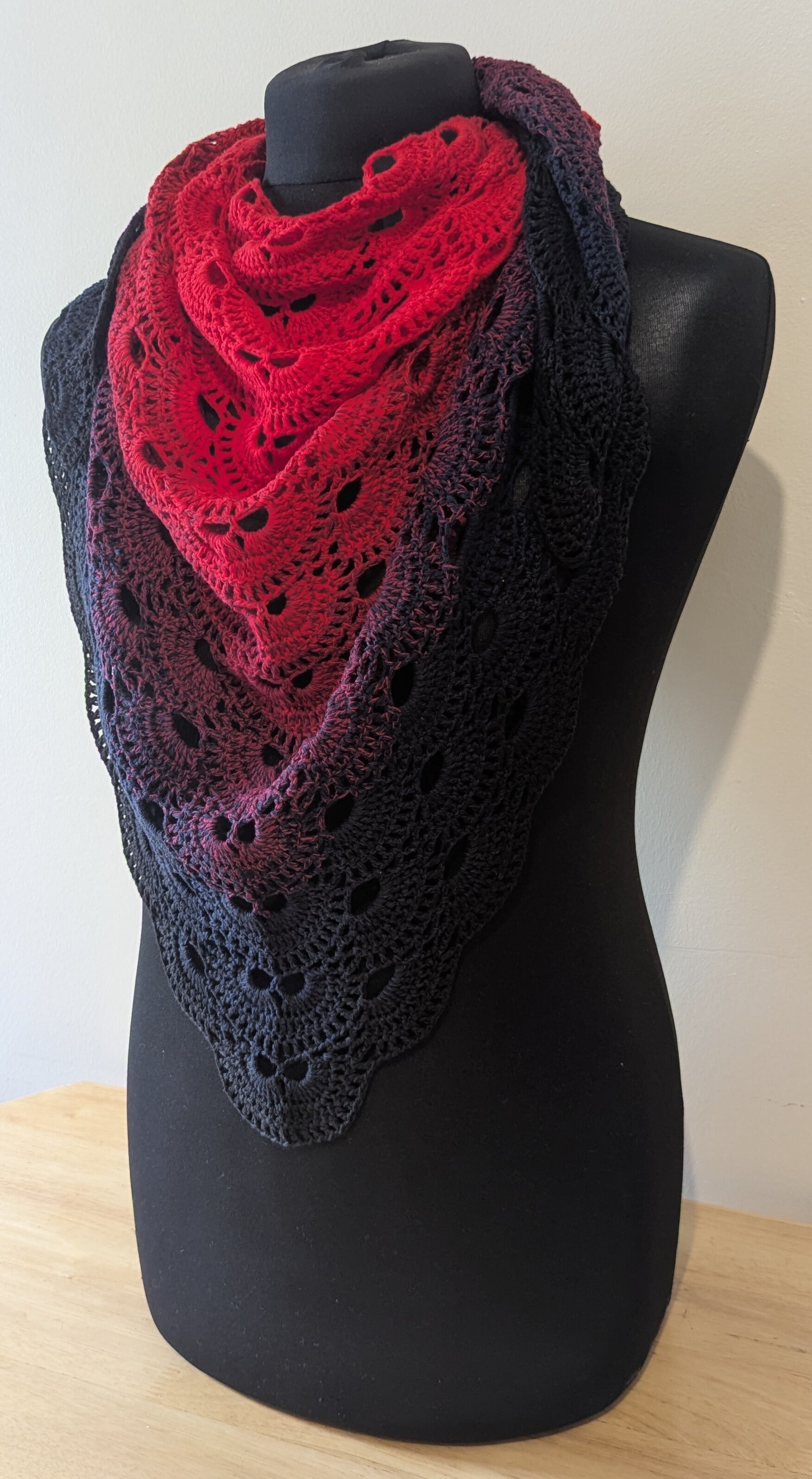 Two-toned red and black crocheted shawl on a black mannequin against a white background