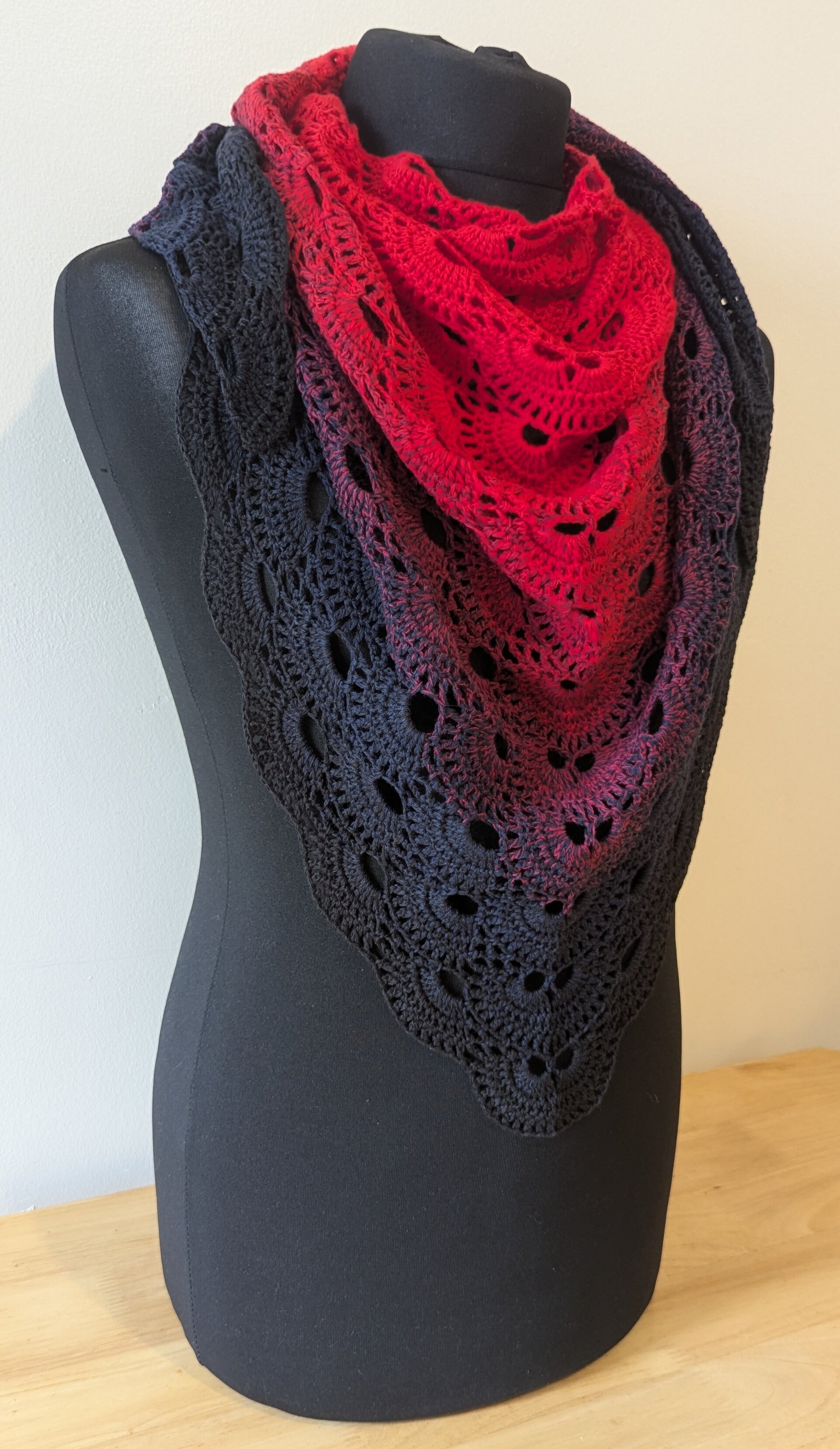 Red and black crocheted shawl on a mannequin against a white background