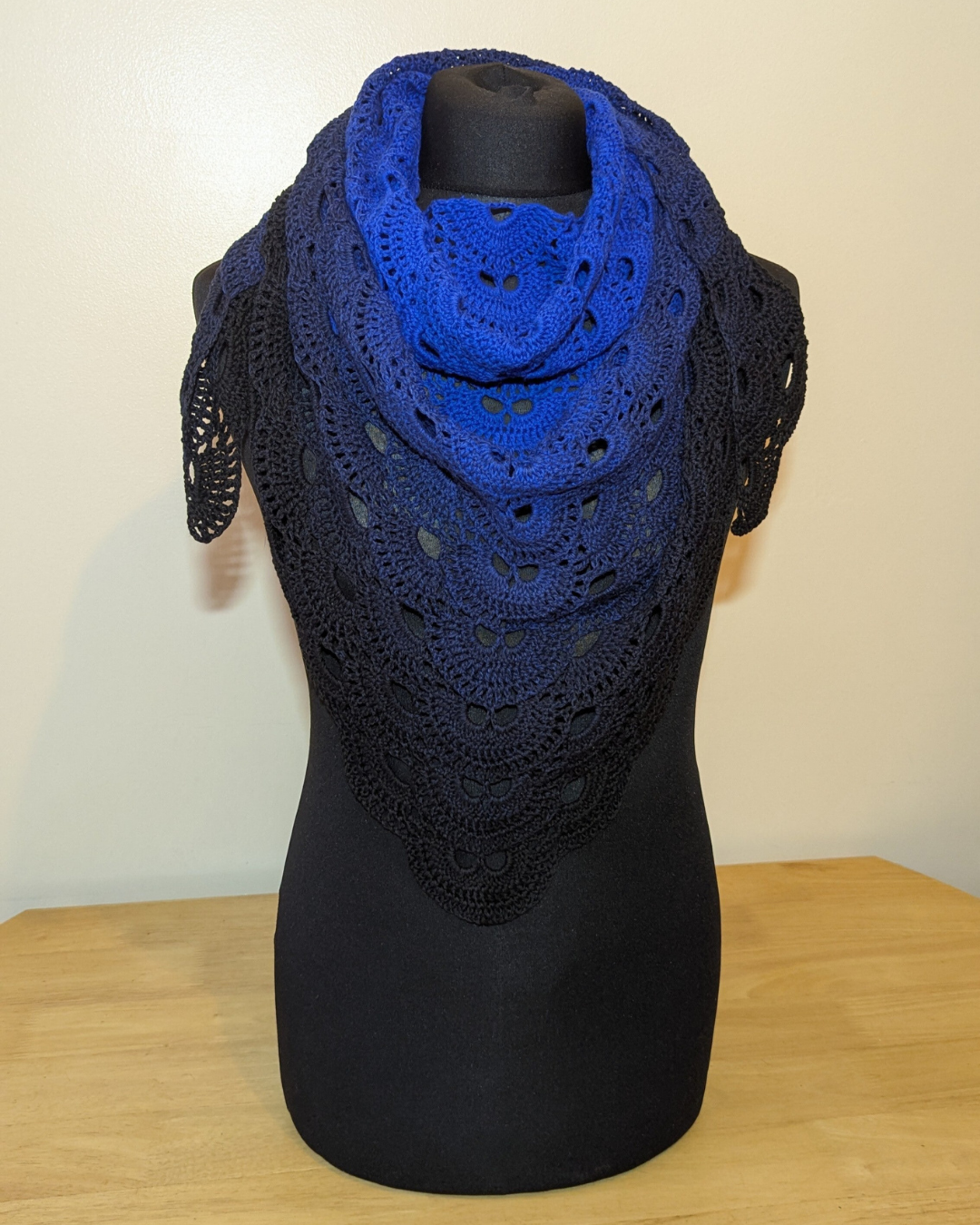 Blue crocheted shawl on a black mannequin against a plain background