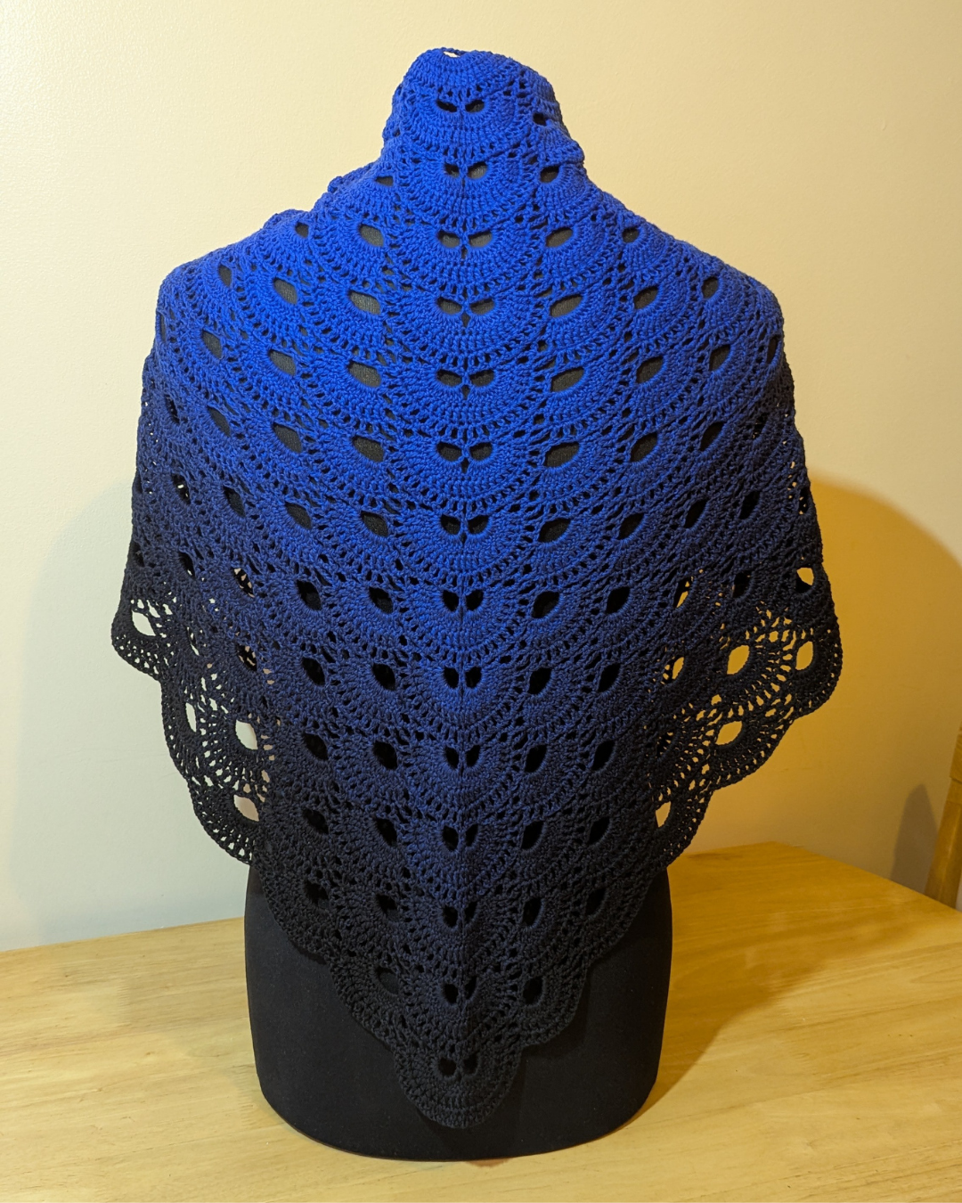 Blue crocheted shawl on a black mannequin against a beige wall.