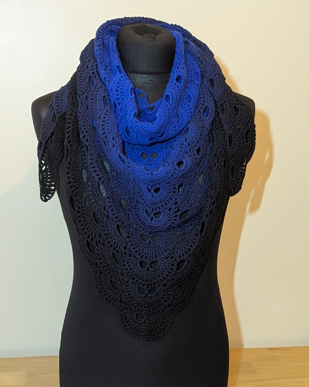 Blue crocheted shawl on a black mannequin against a white background