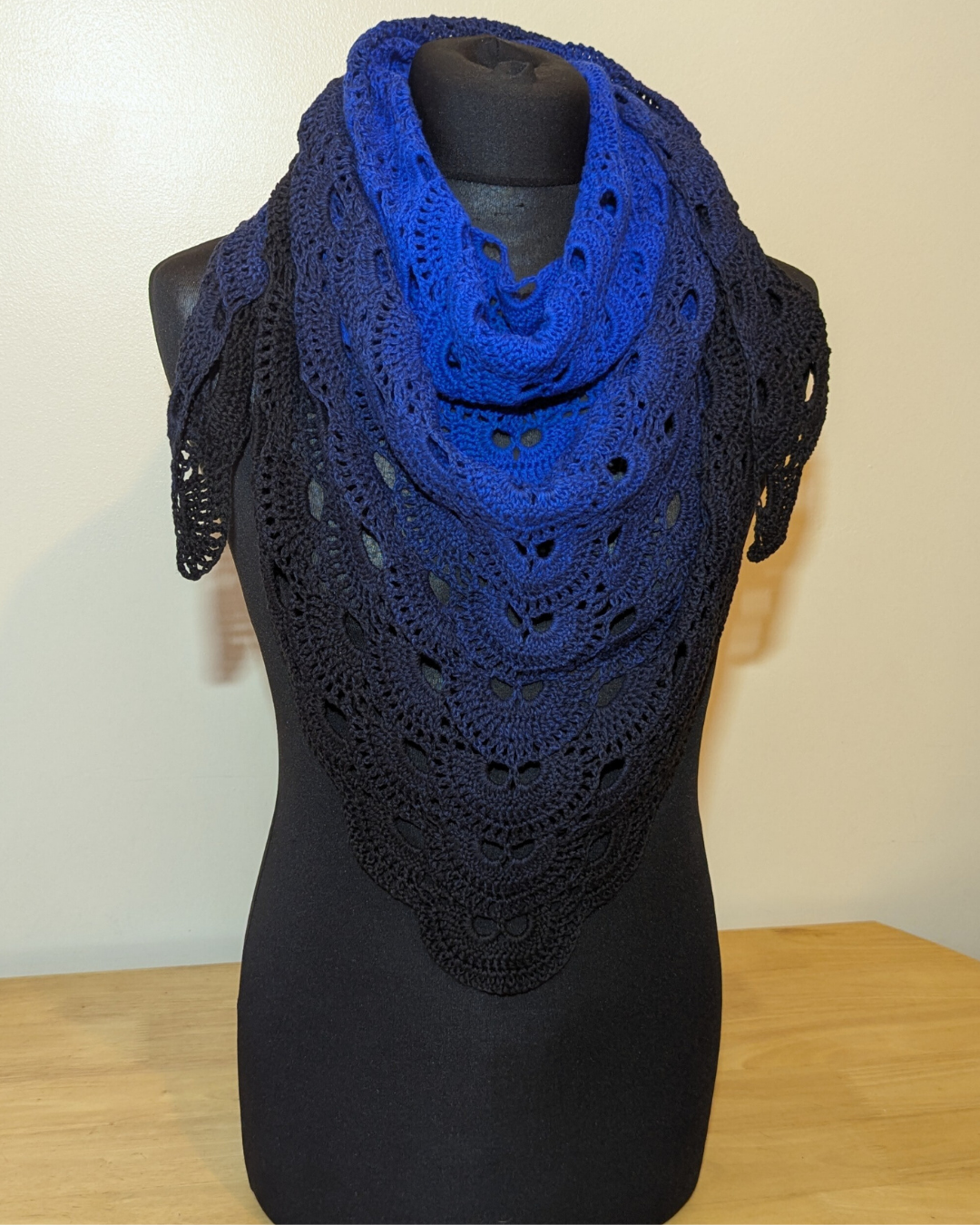 Blue crocheted shawl on a black mannequin against a white background
