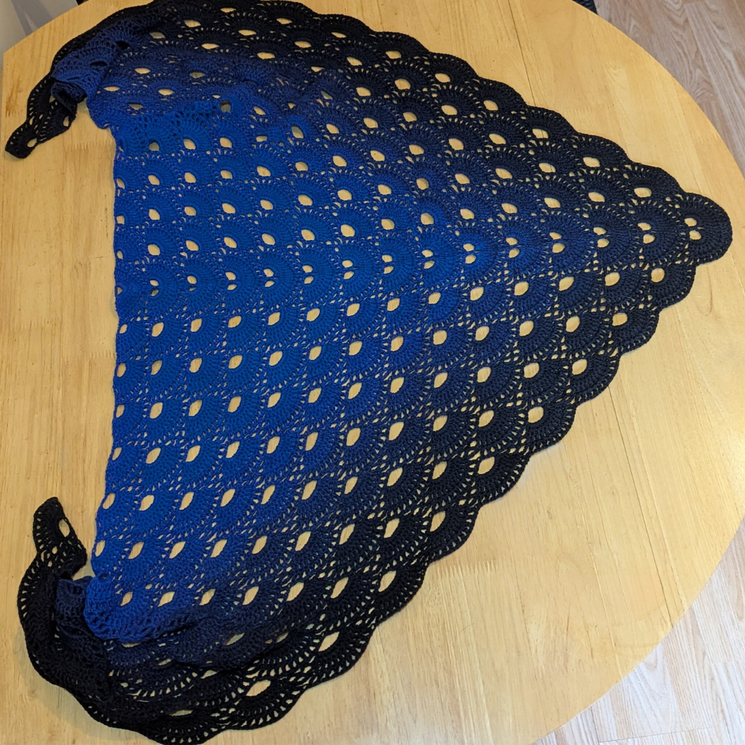 Blue gradient shawl with scalloped edge on a wooden table
