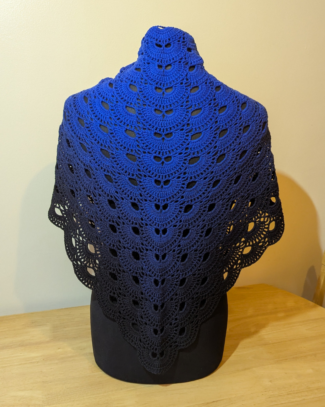 Blue crocheted shawl on a black mannequin against a beige wall.